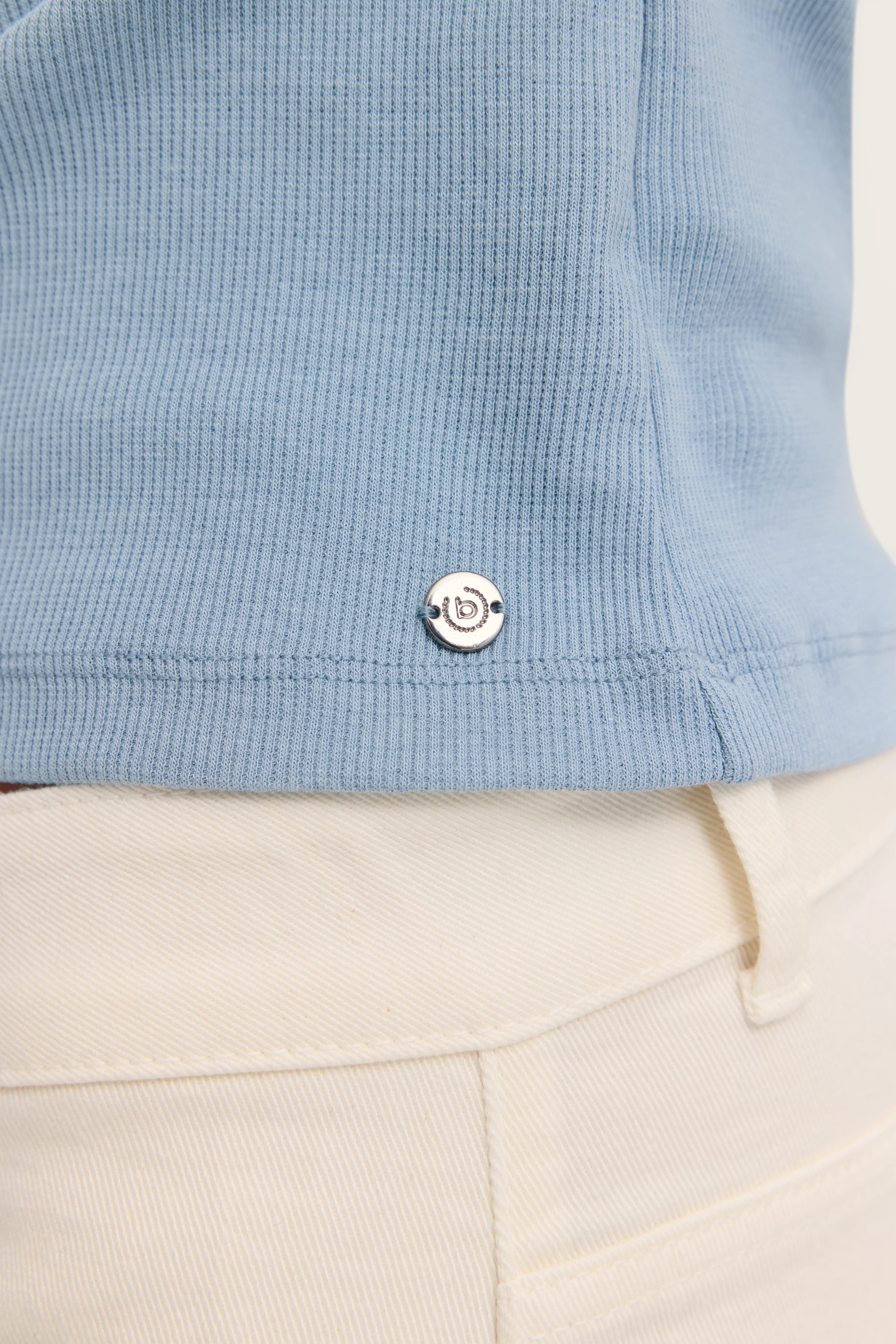 Blaues geripptes T-Shirt Detail mit bugatti Logo, kombiniert mit cremefarbener Hose.