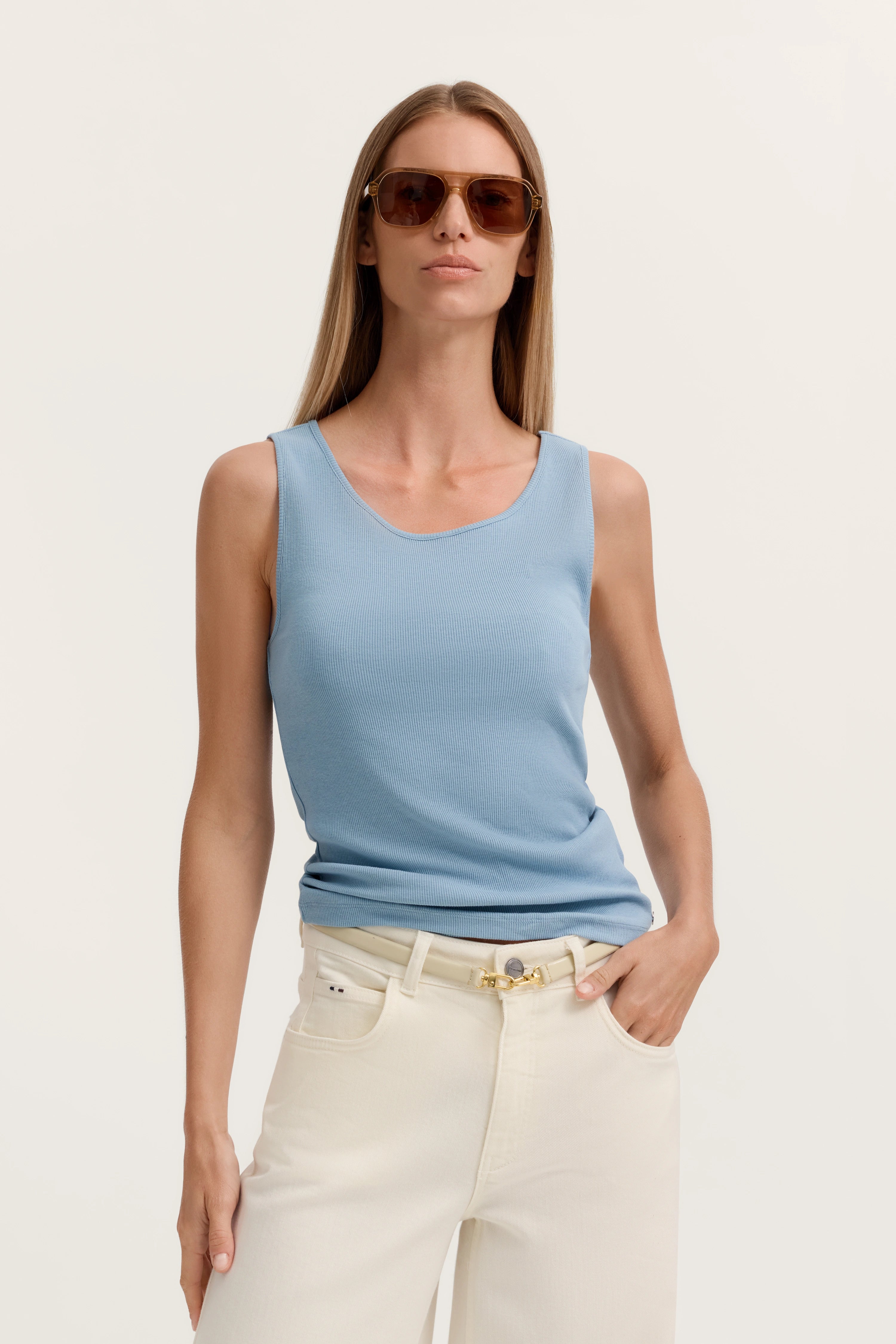 Model in hellblauem Top und weißen Hosen, lässige Pose, Sonnenbrille, bugatti Stil.