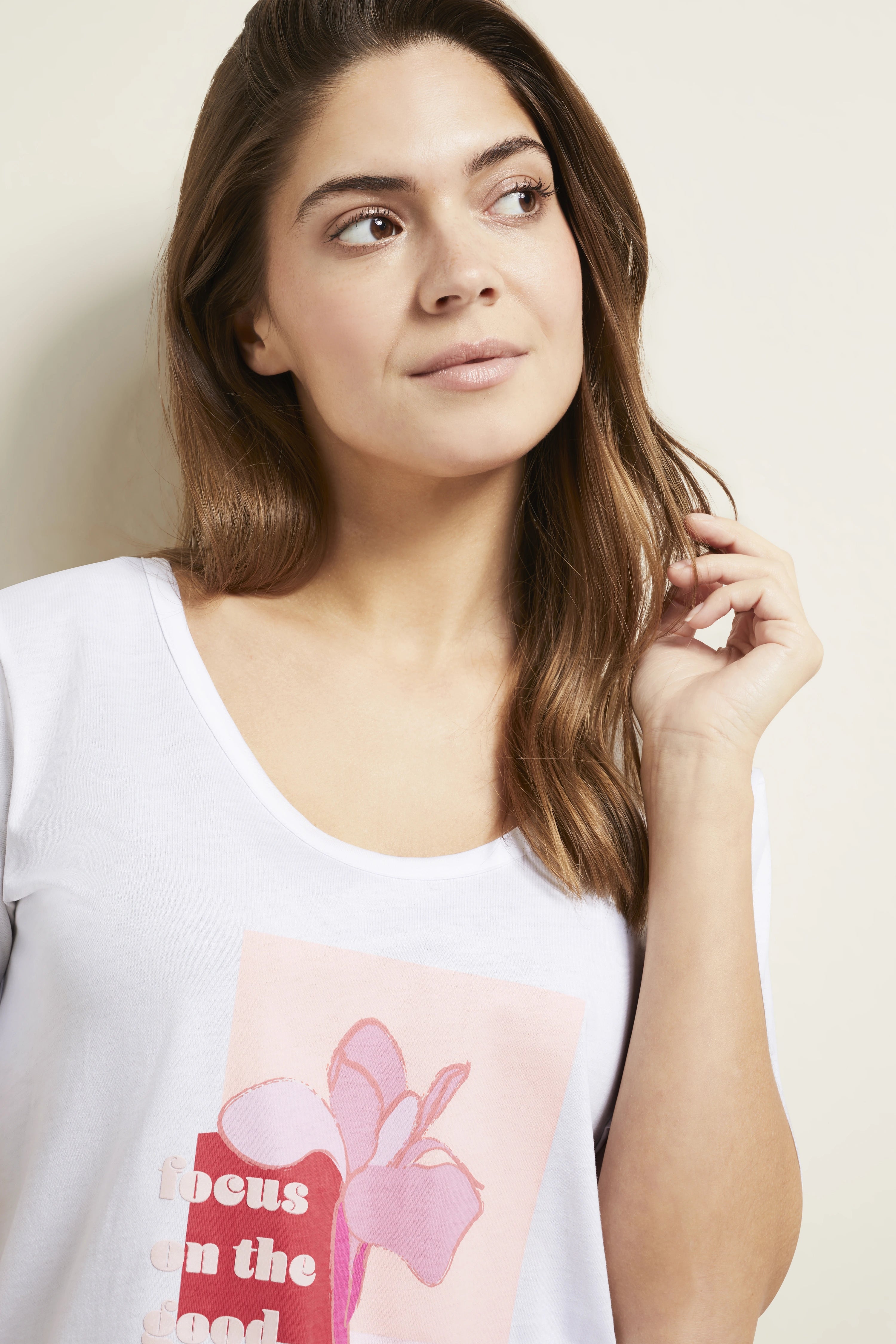 Model trägt weißes bugatti Shirt mit rosa Print, legere Pose, Blick zur Seite.