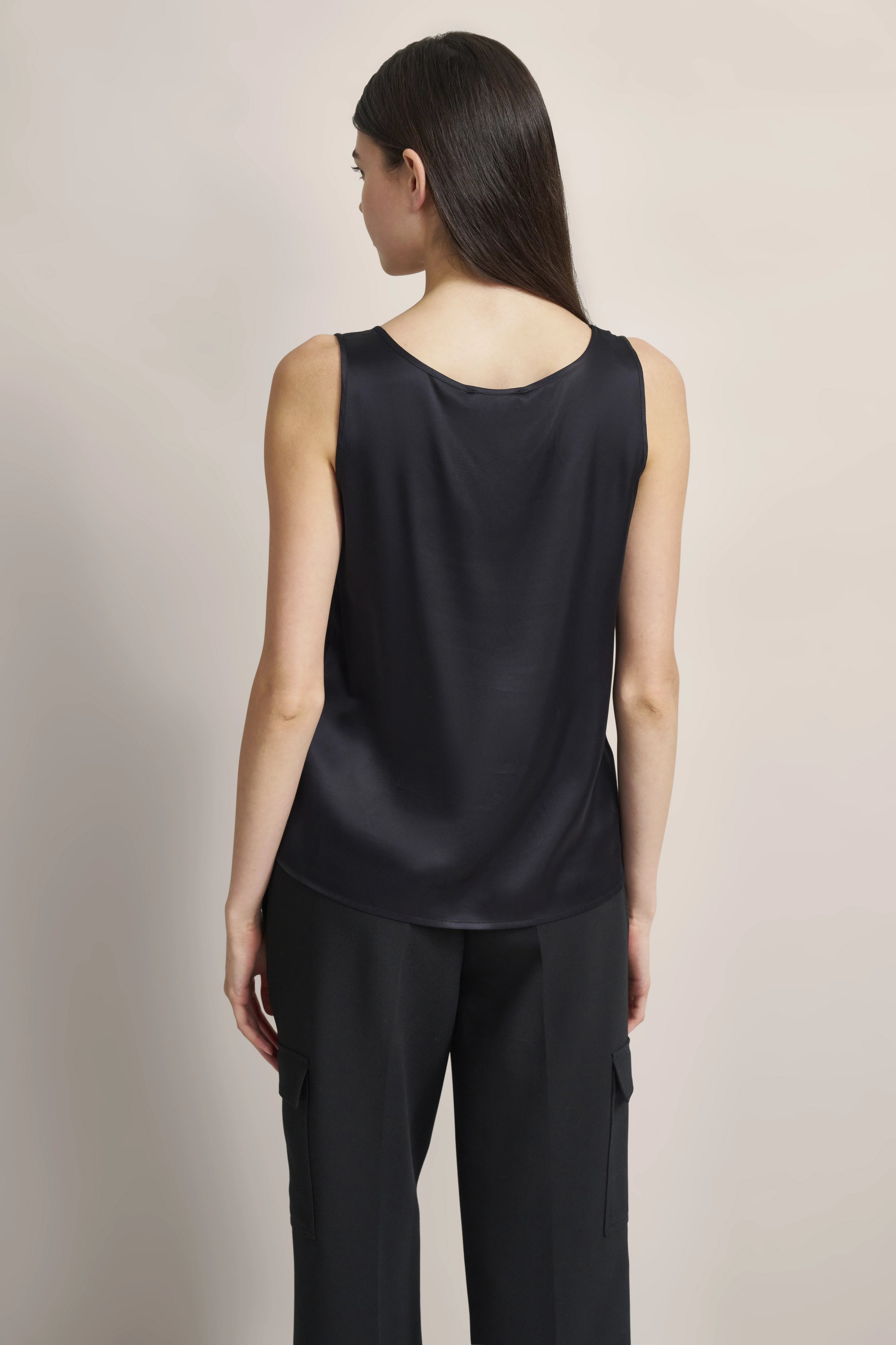 Ärmelloses schwarzes Top mit weiter schwarzer Hose, Rückansicht, Model in entspanntem Stand.