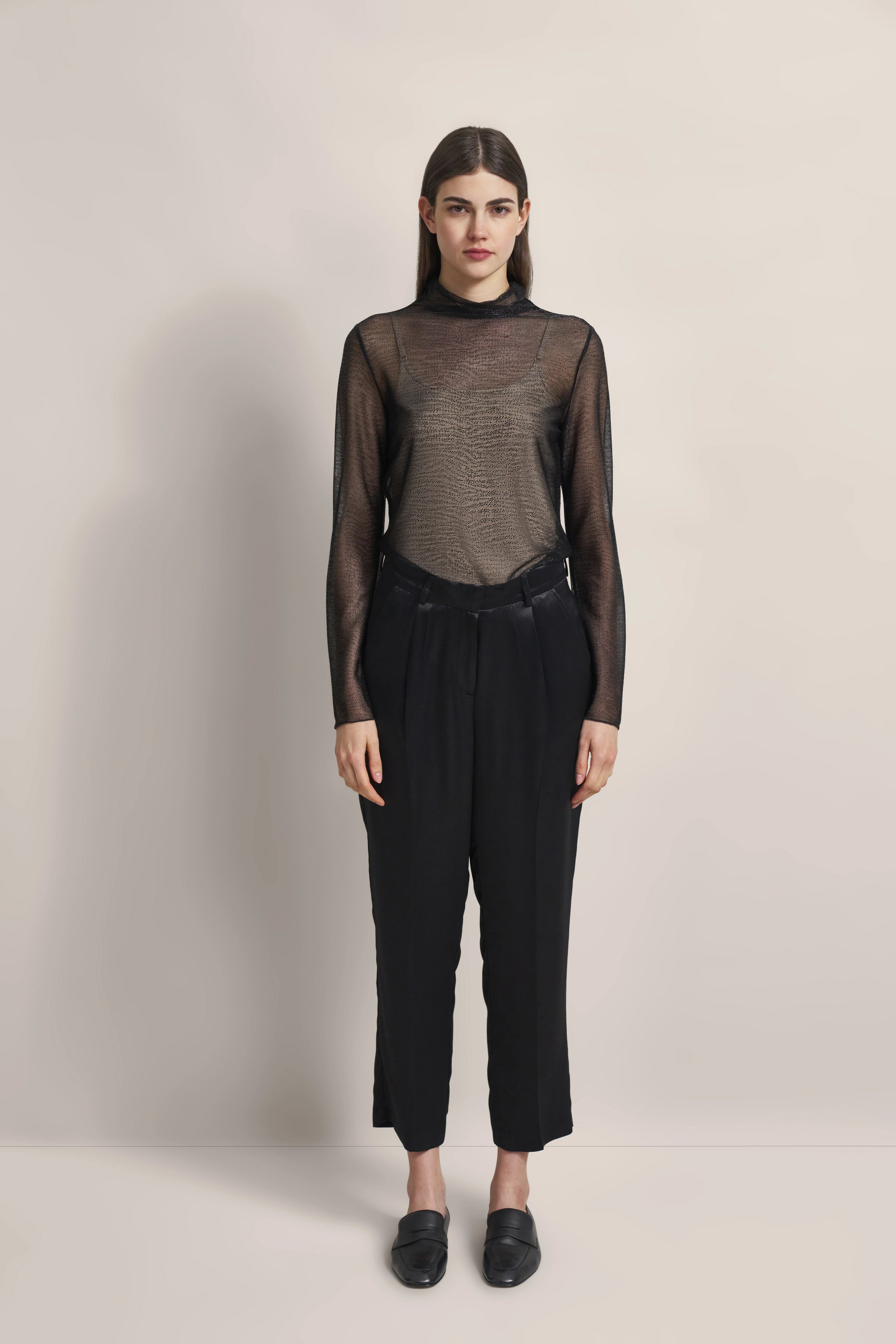 Schwarzes transparentes Langarmshirt, schwarze Hose, Model steht frontal, elegantes Outfit.