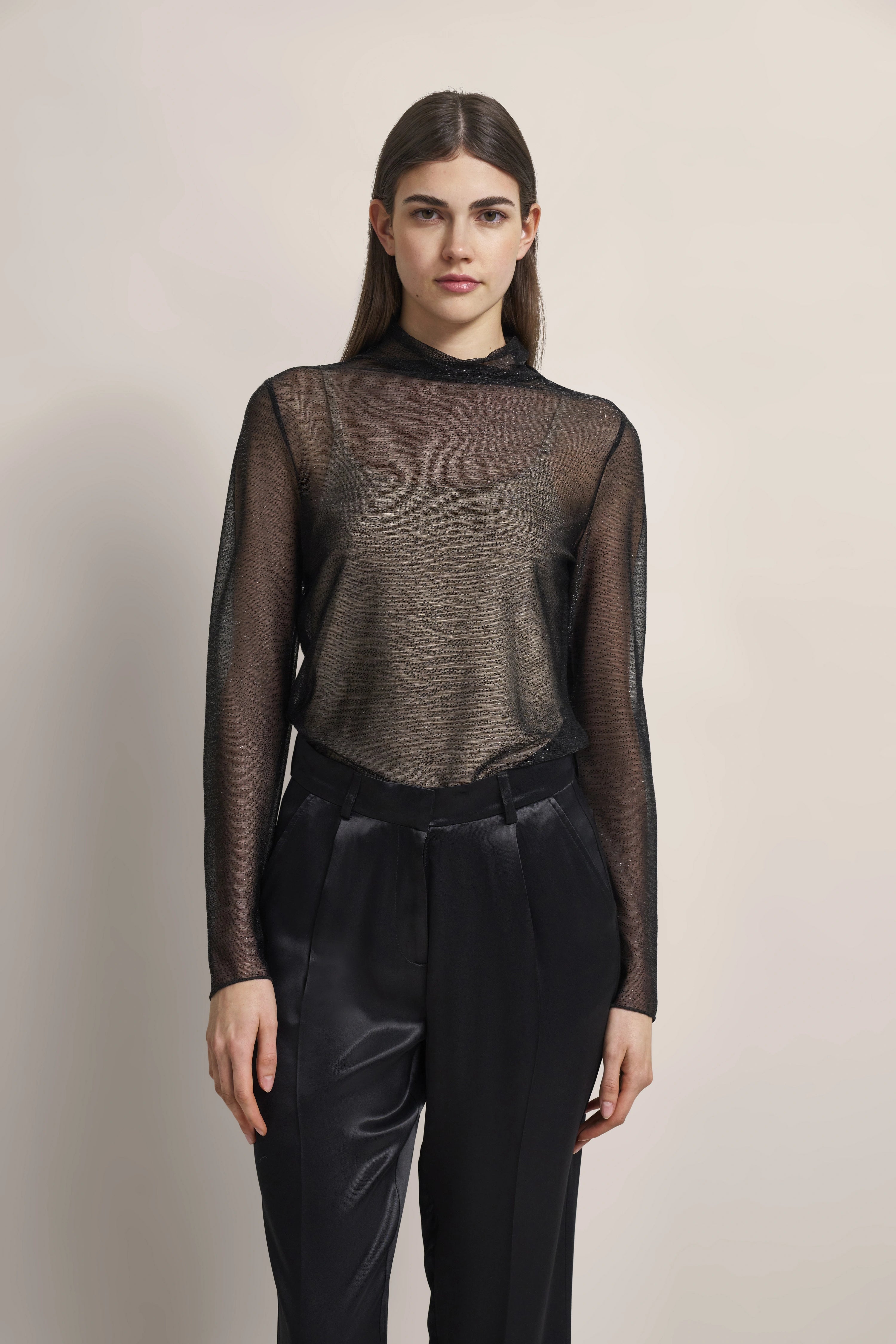 Modelbild in schwarzem, transparentem Oberteil und schwarzen Hosen, frontal, entspannt stehend.