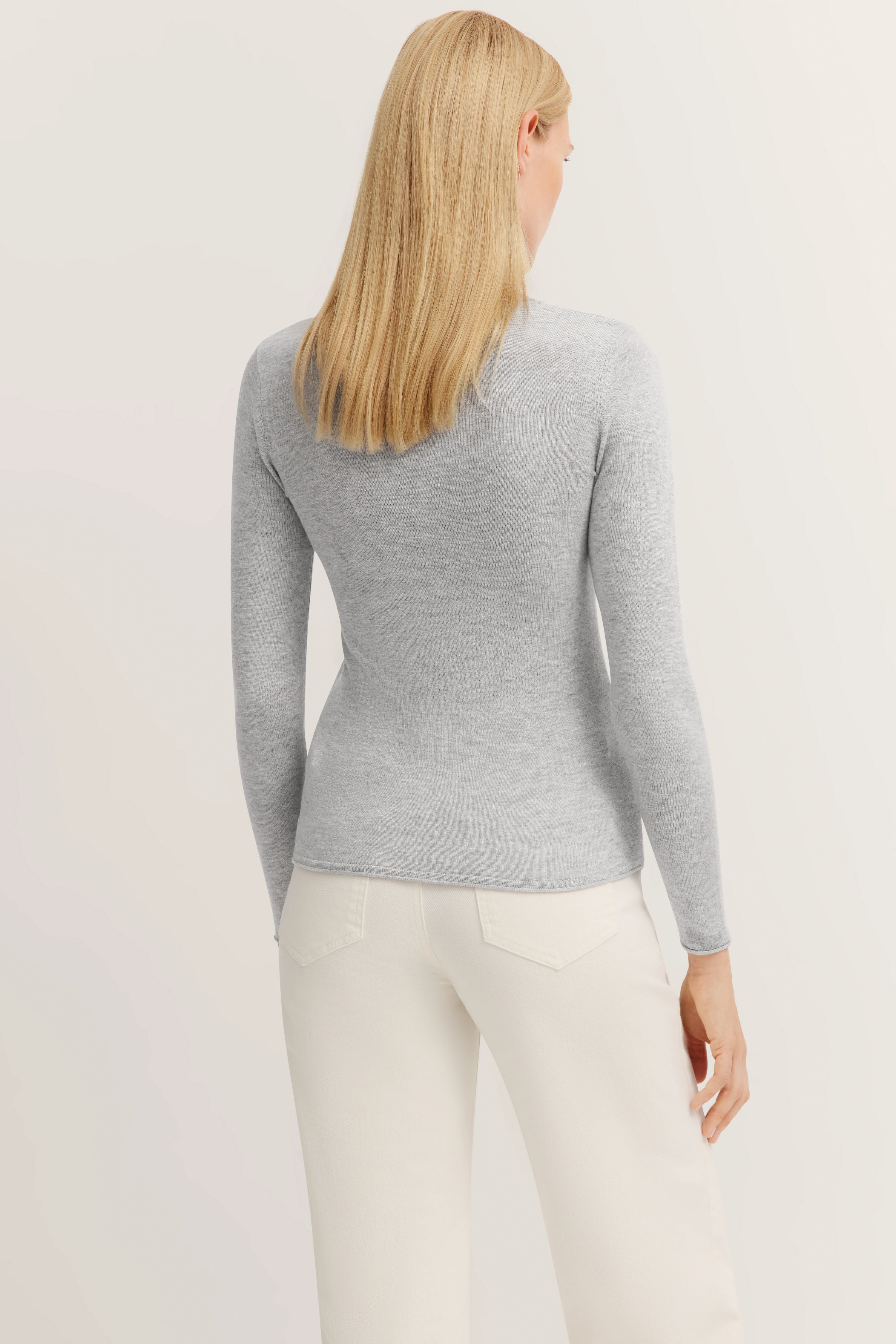 Grijze trui met lange mouwen en witte broek, model van achteren, ontspannen houding, bugatti stijl.