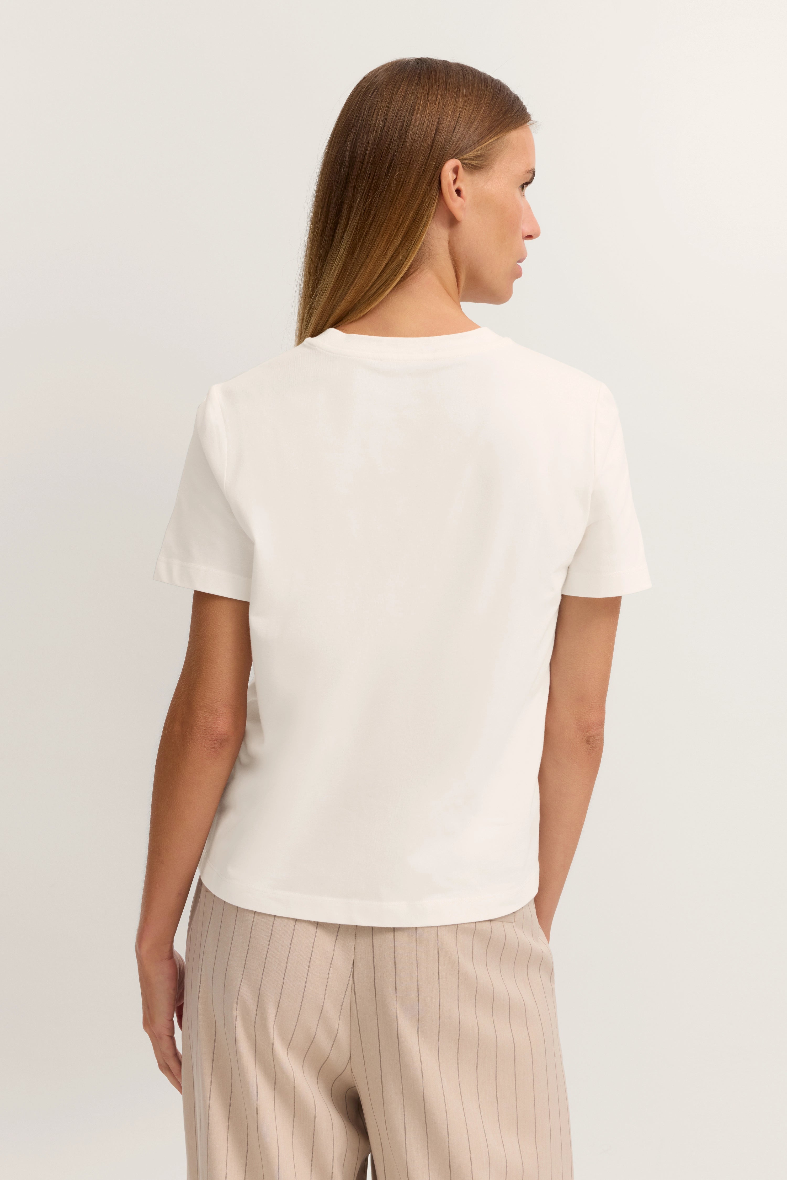 Weißes T-Shirt und beige gestreifte Hose, Rückansicht eines Models, lässige Pose.