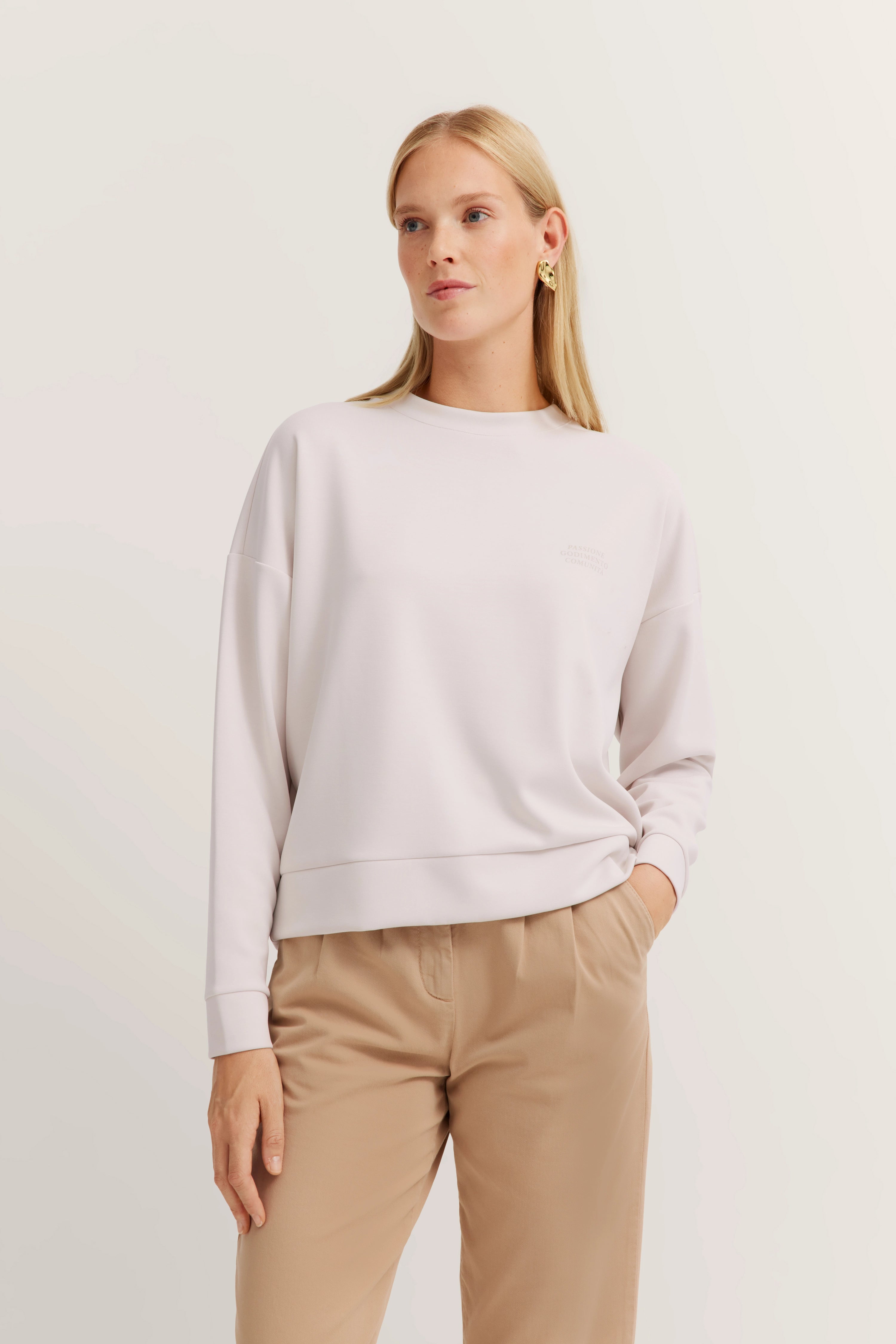 Damesoutfit: Witte trui en beige broek, casual modelbeeld, ontspannen pose.