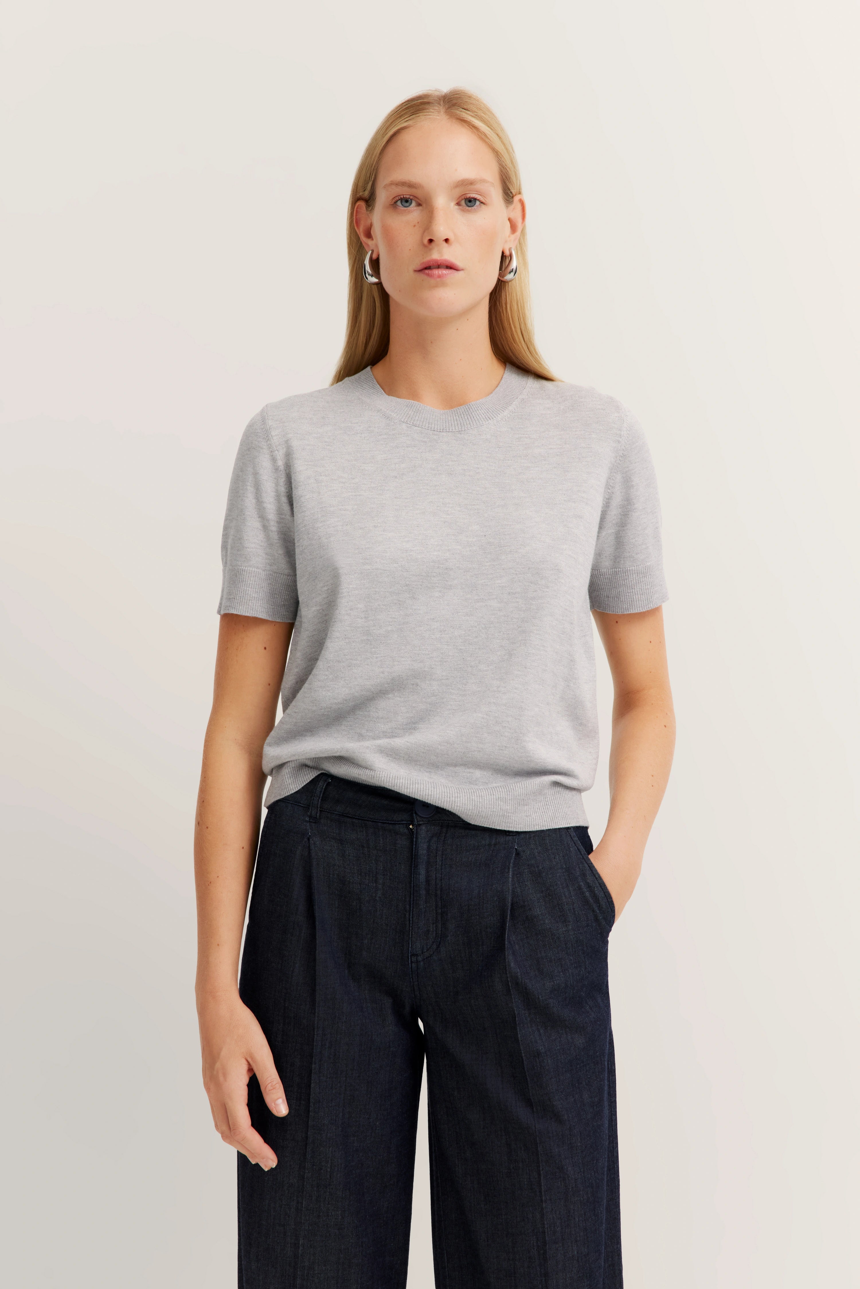 Grijs T-shirt en donkerblauwe broek, ontspannen model, natuurlijke pose.