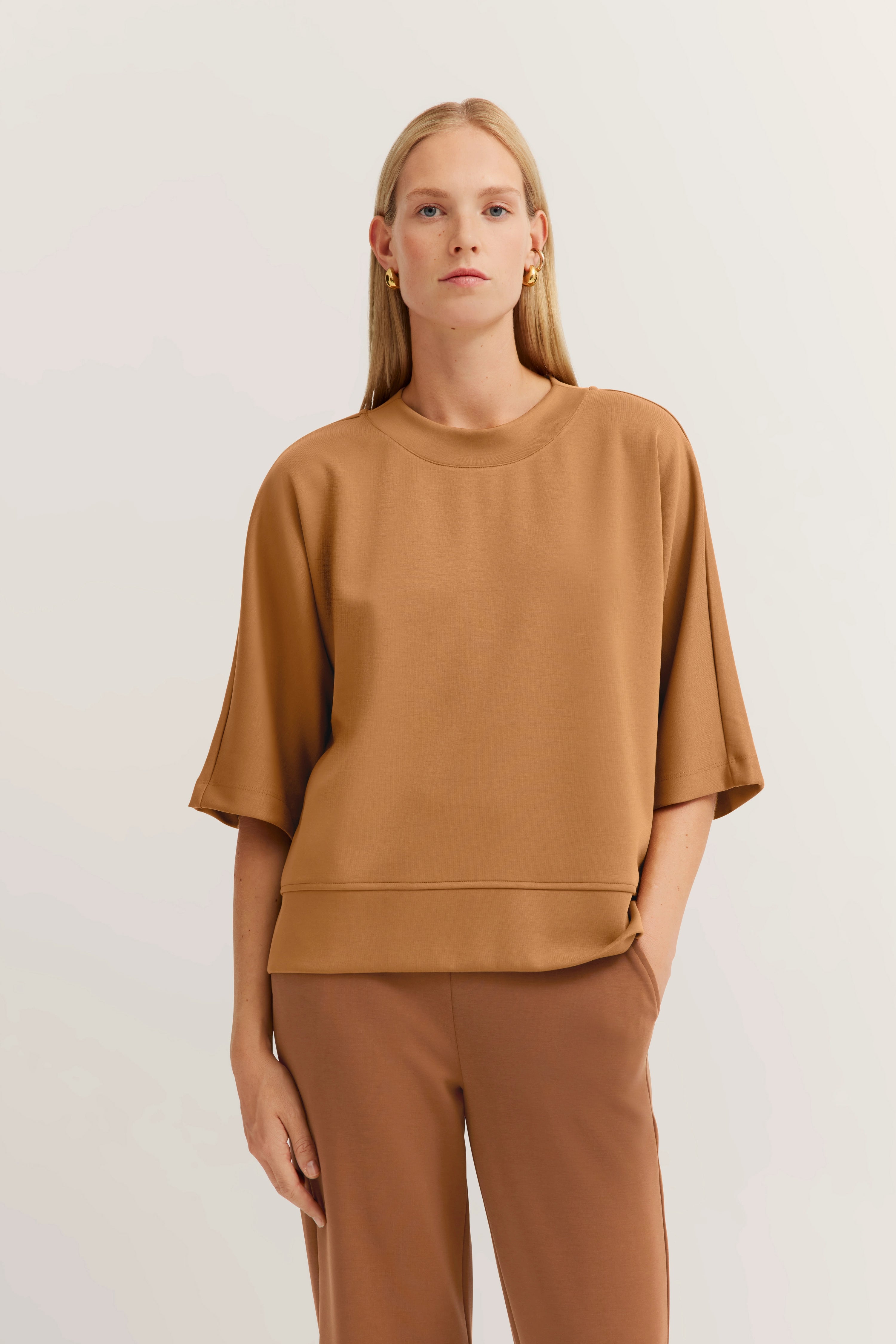 Model in camel outfit, nonchalant poserend met hand in zak, bugatti elegantie en comfort.