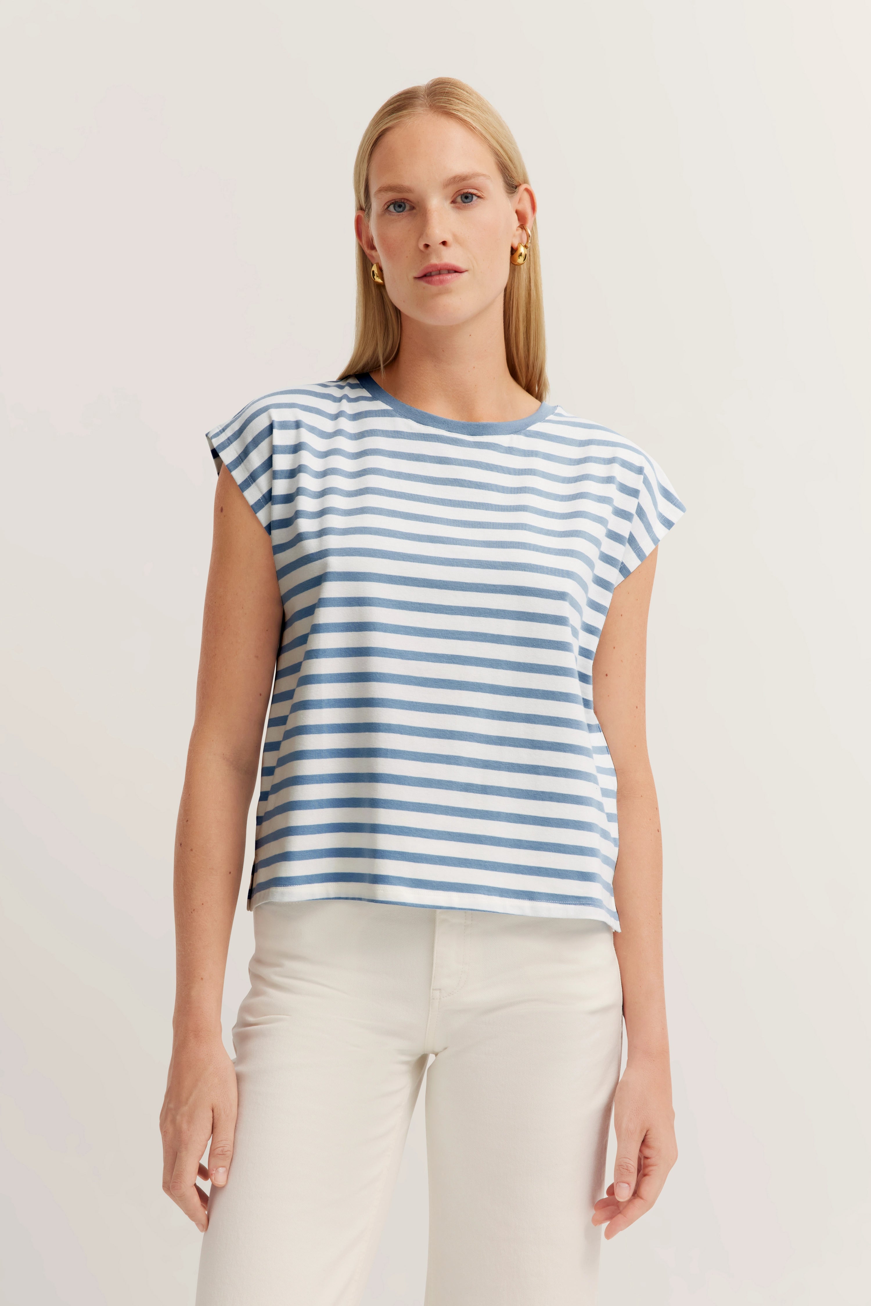 Gestreept blauw-wit top op model met witte broek, ontspannen pose.