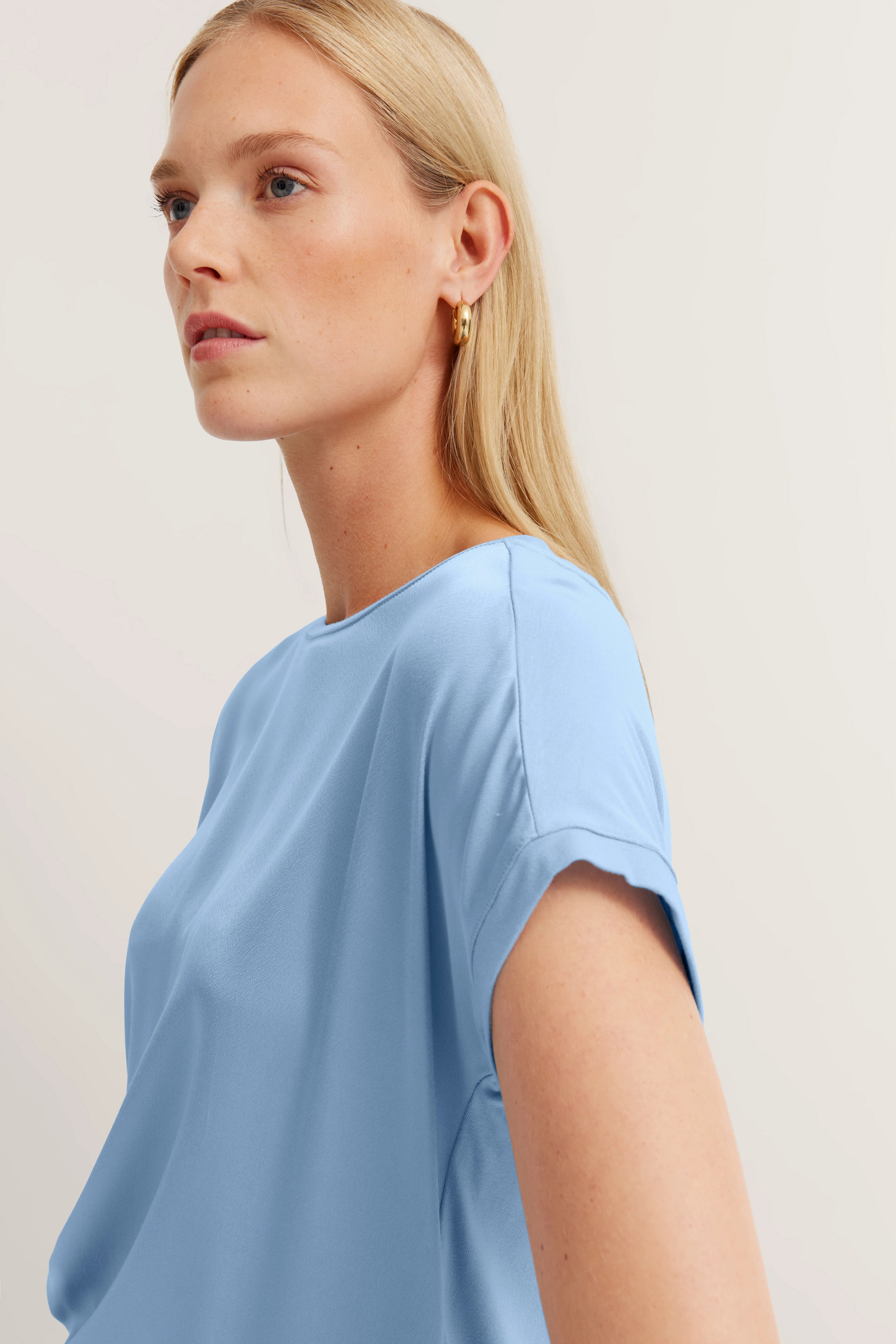 Blaues bugatti Oberteil auf Model, seitliches Porträt, entspannter Look, goldene Ohrringe.