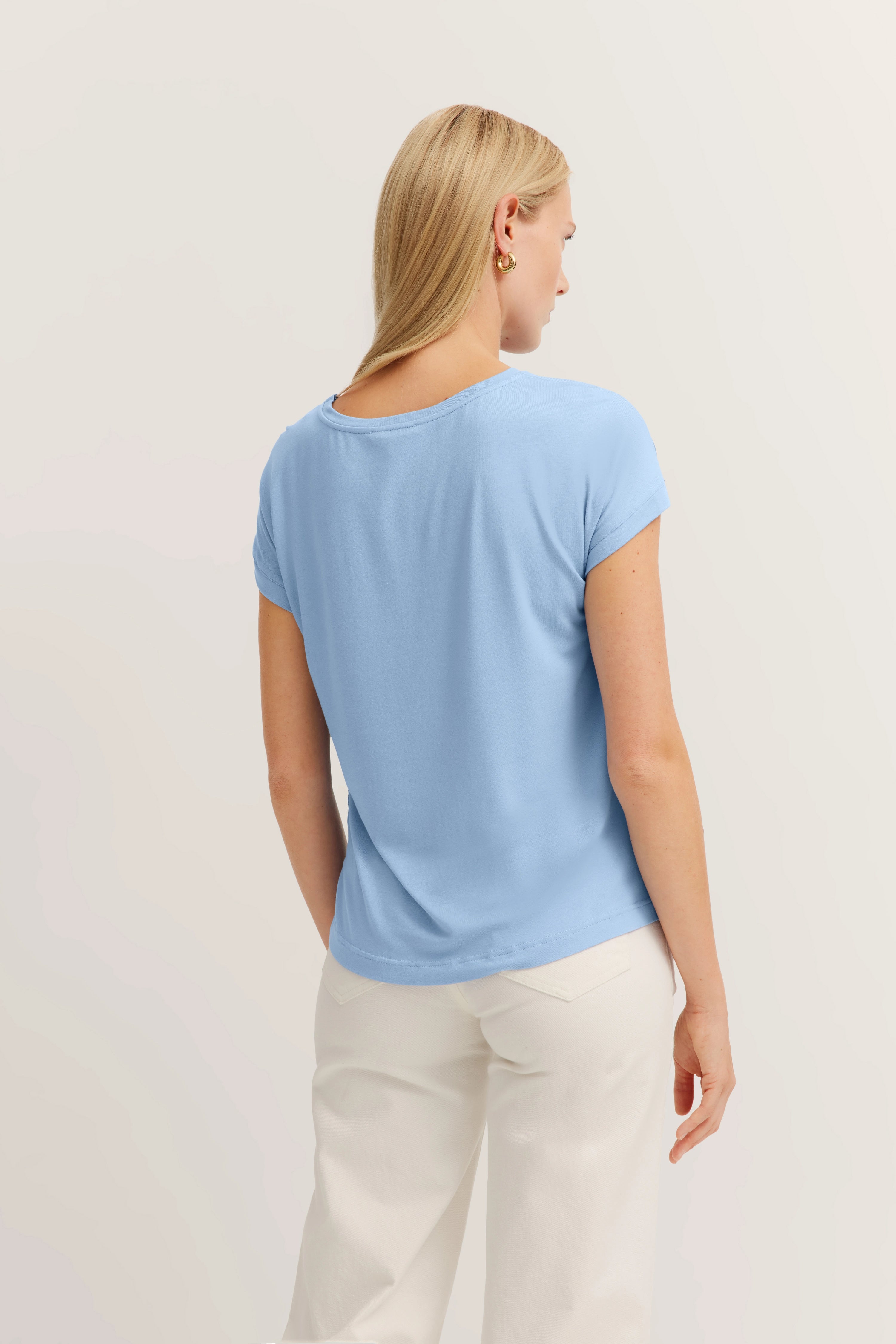 Blaues T-Shirt und weiße Hose, Model von hinten, lässige Pose.