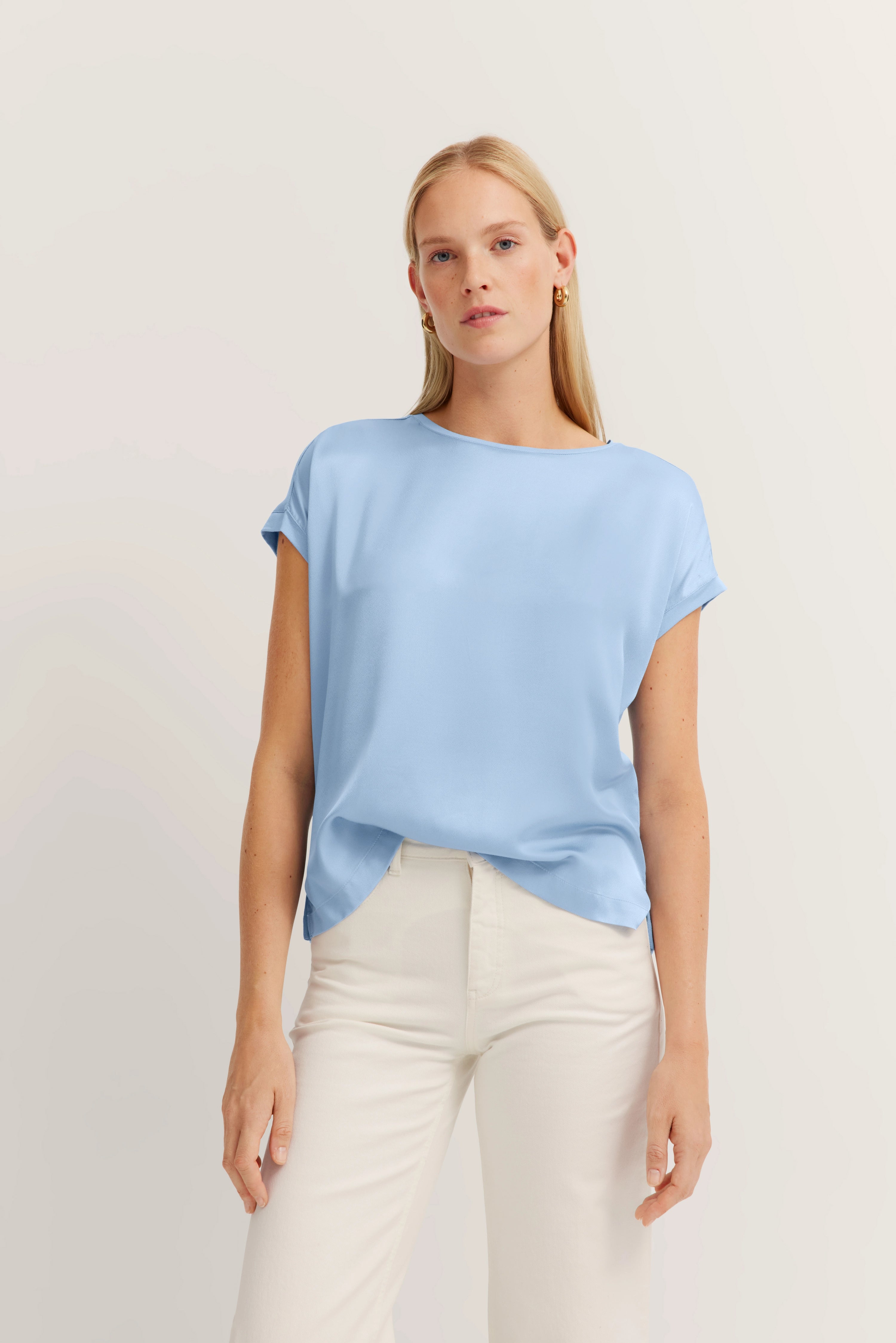 Blaues bugatti T-Shirt, weißer Hosen-Modelbild, entspanntes Posing.