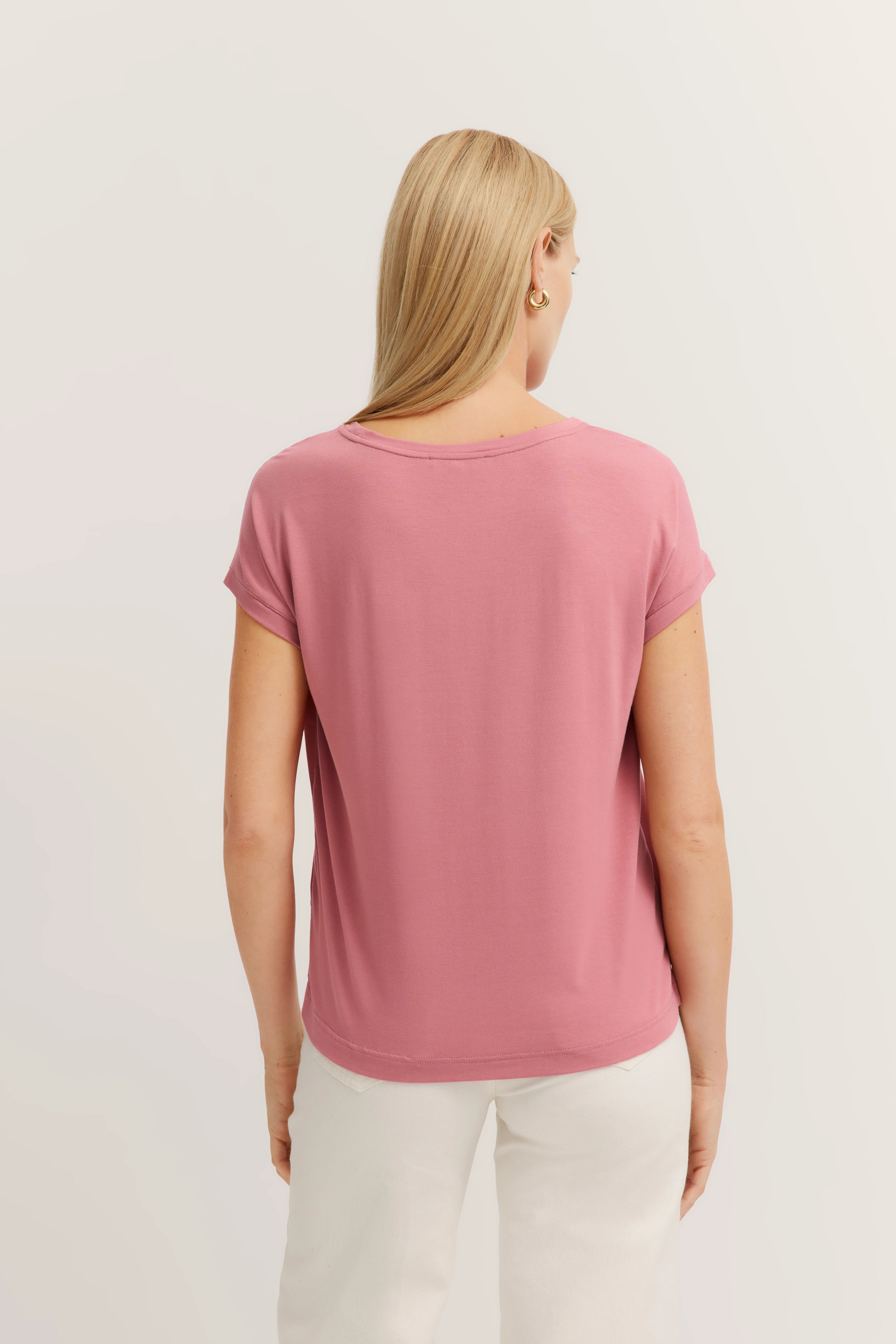 Achteraanzicht model in roze bugatti shirt en witte broek, casual stijl, ontspannen houding.