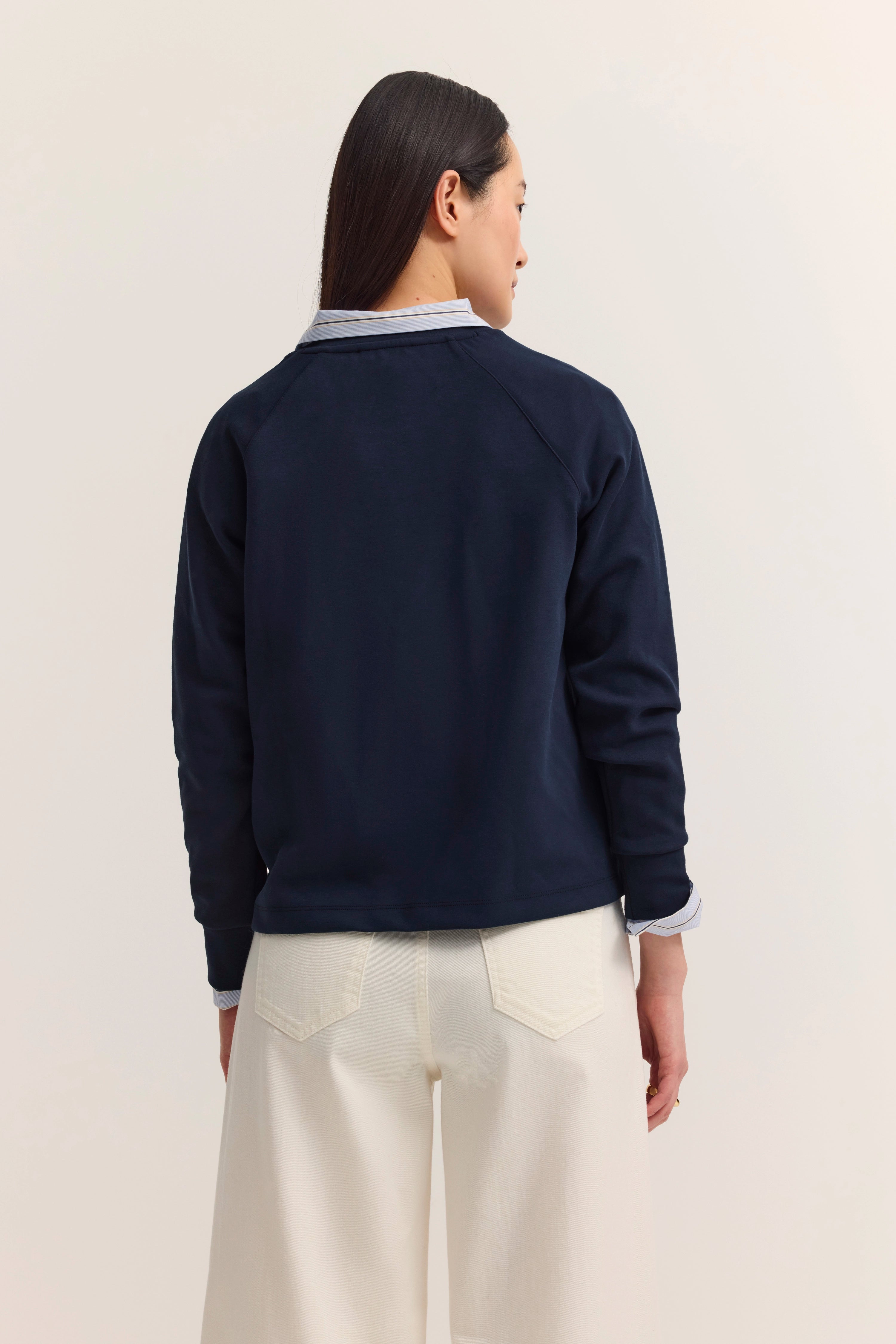 bugatti Outfit: Dunkelblauer Pullover, weiße Hose, legeres Modelbild, Rückansicht.