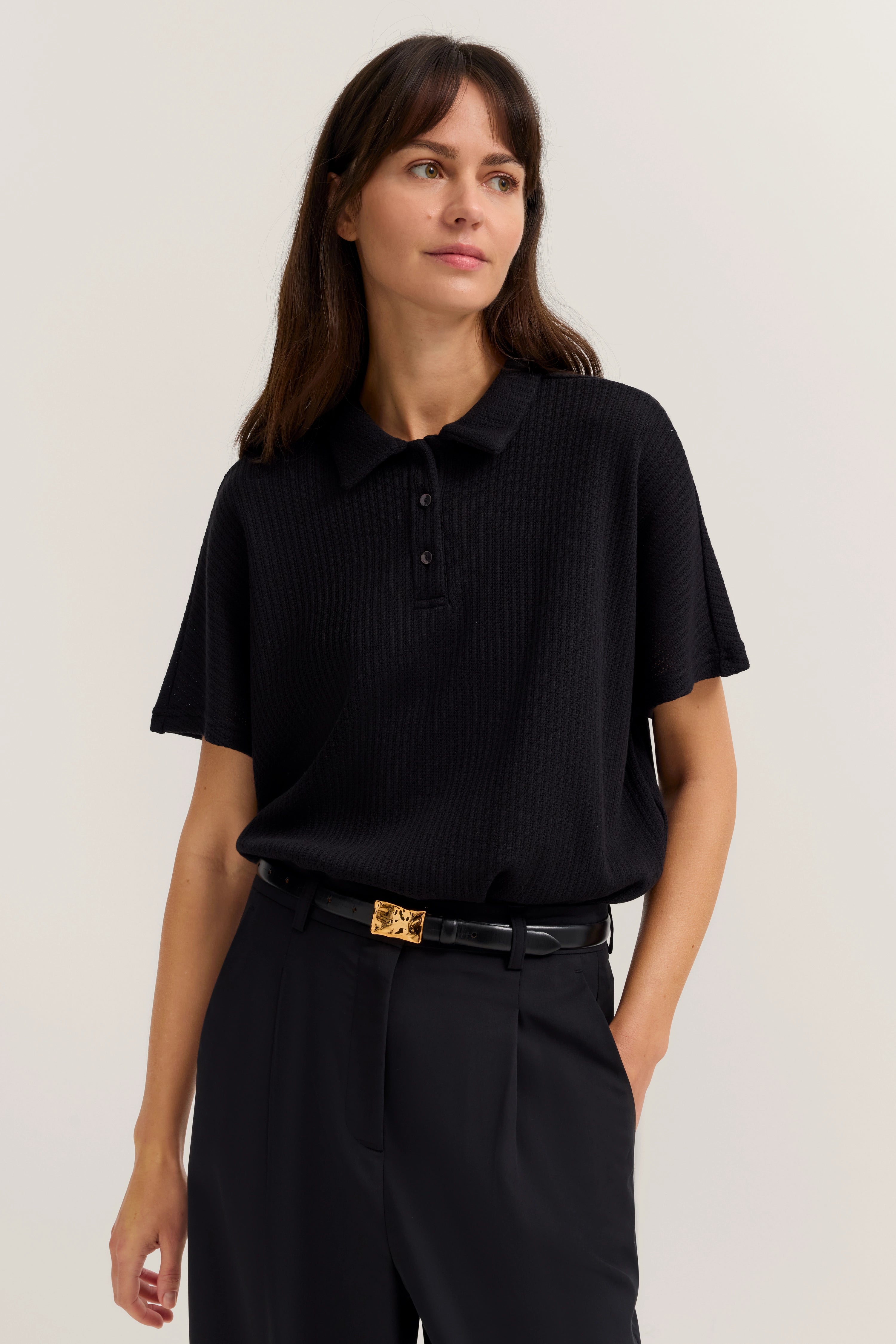 Schwarzes Polohemd und Hose, legeres Modelbild, entspannte Pose.