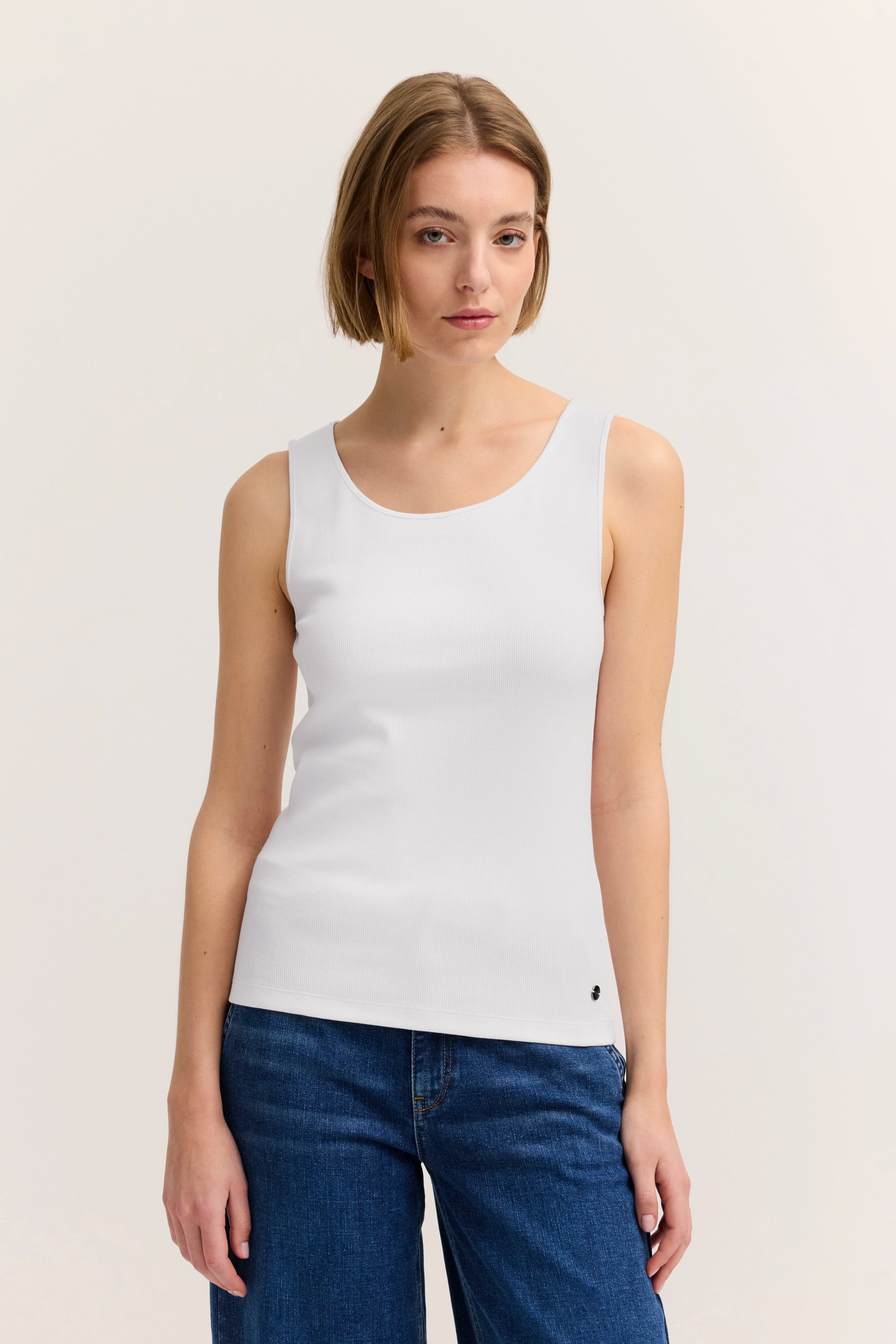 Weißes ärmelloses Top und blaue Jeans, Modelbild, entspannte Pose.