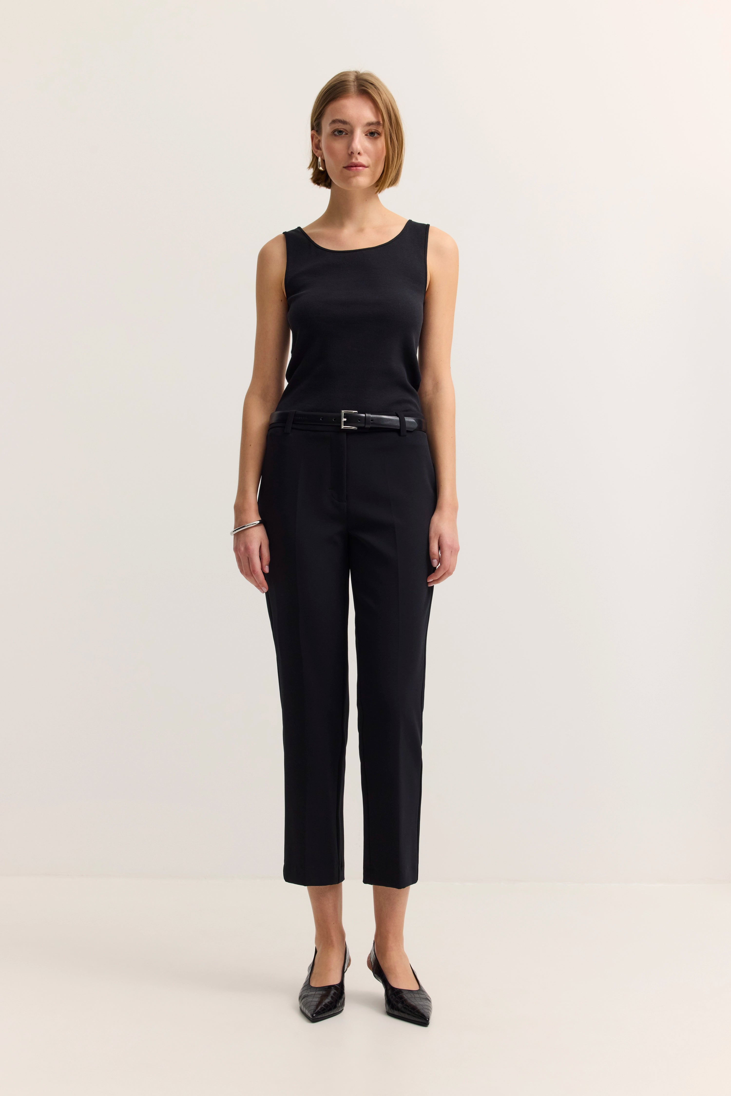 Schwarzes ärmelloses Top und Hose, Model steht frontal, schlichtes Posing.