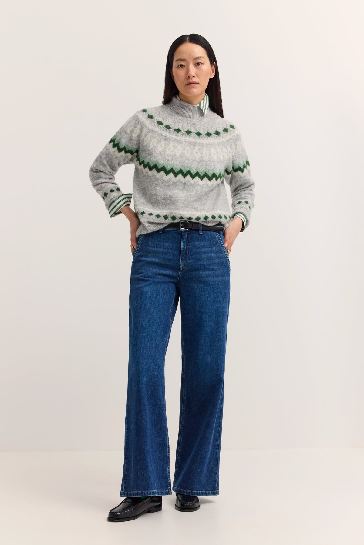 Grauer Pullover mit grünem Muster, blaue Jeans, Model mit lässigem Posing.