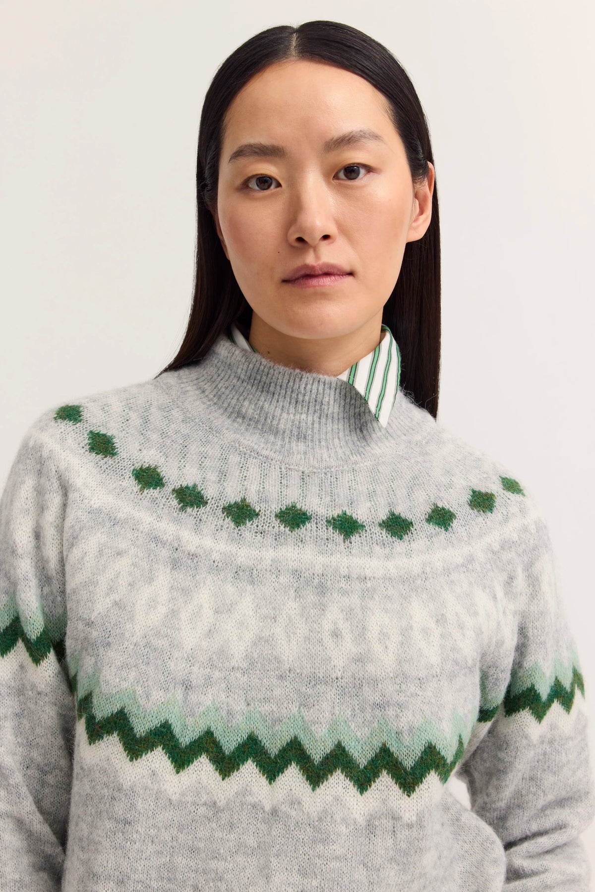 Grauer Pullover mit grünem Muster, gestreiftes Hemdkragen-Detail, Modelbild, entspanntes Posing.