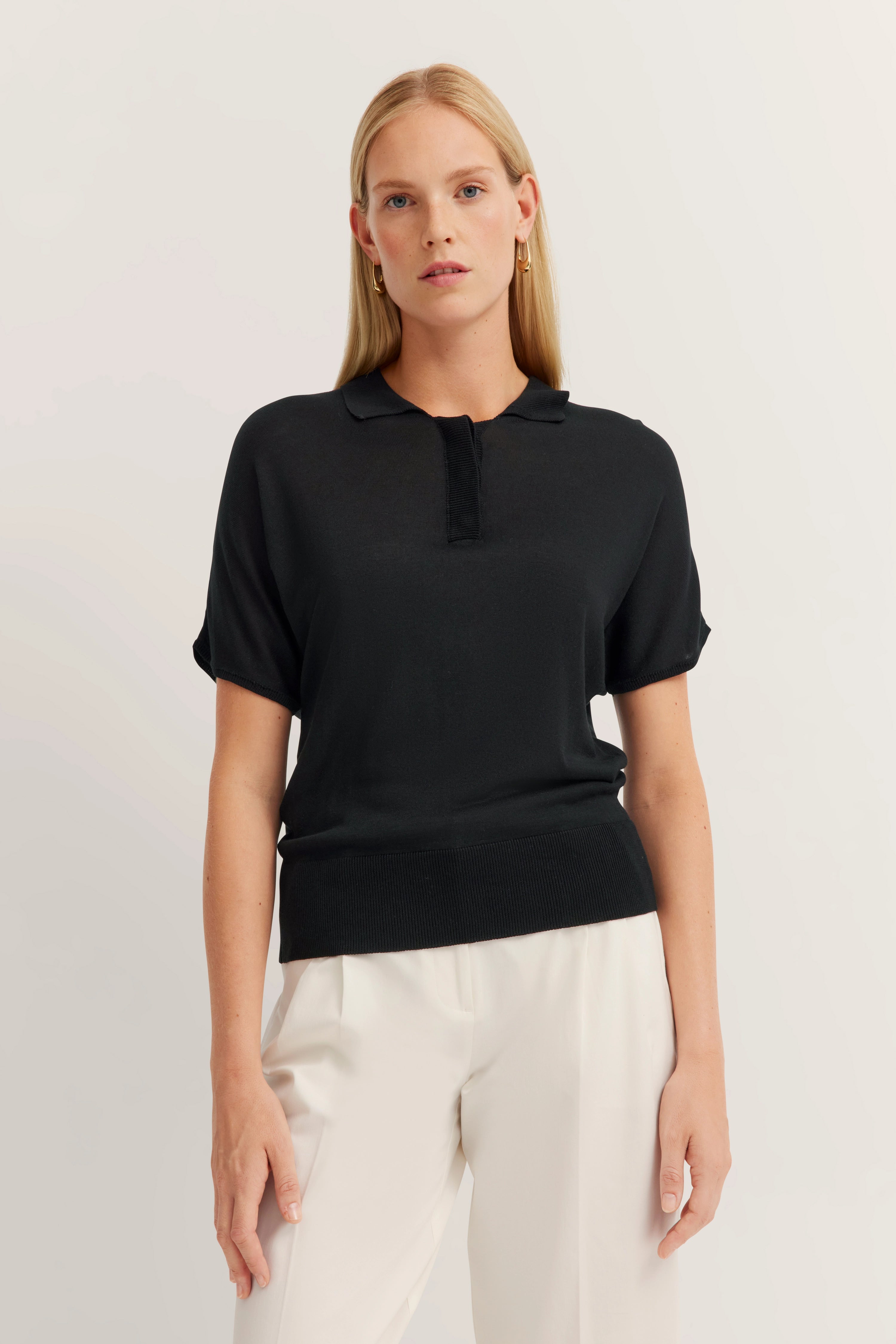 Schwarzer bugatti Poloshirt, weißer Bugatti Hose, Model stehend, entspannter Ausdruck.
