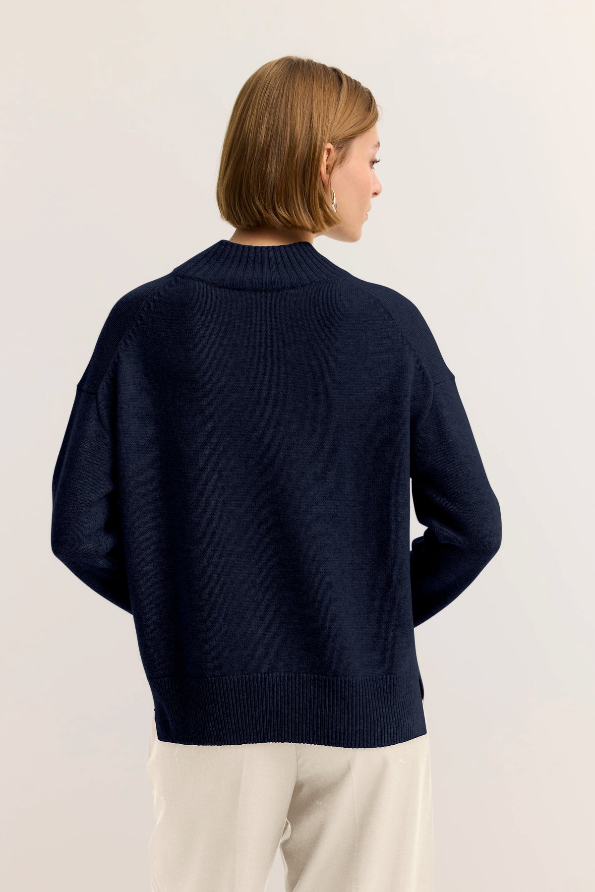 Model in dunkelblauem bugatti Pullover, Rückansicht, lässiges Pose, cremefarbene Hose.