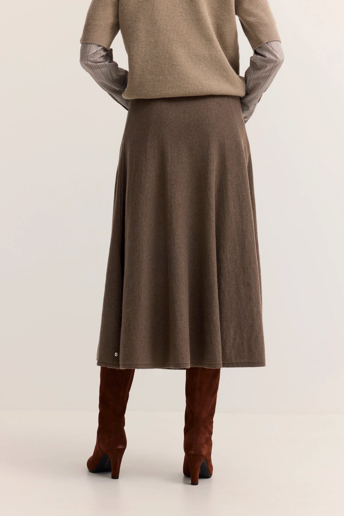 Brauner bugatti Rock, beige Pullover, gestreifte Ärmel, braune Stiefel, legeres Modelbild, Rückenansicht.