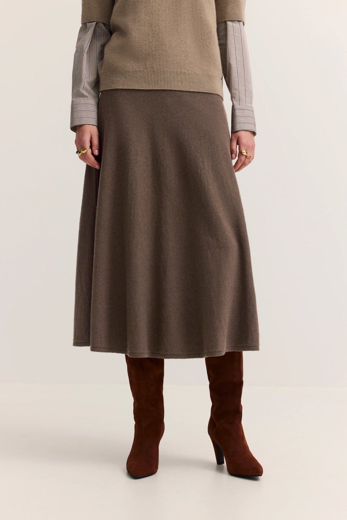 Brauner Rock, beige Pullover, gestreifte Ärmel, braune Stiefel. Büstenbild.