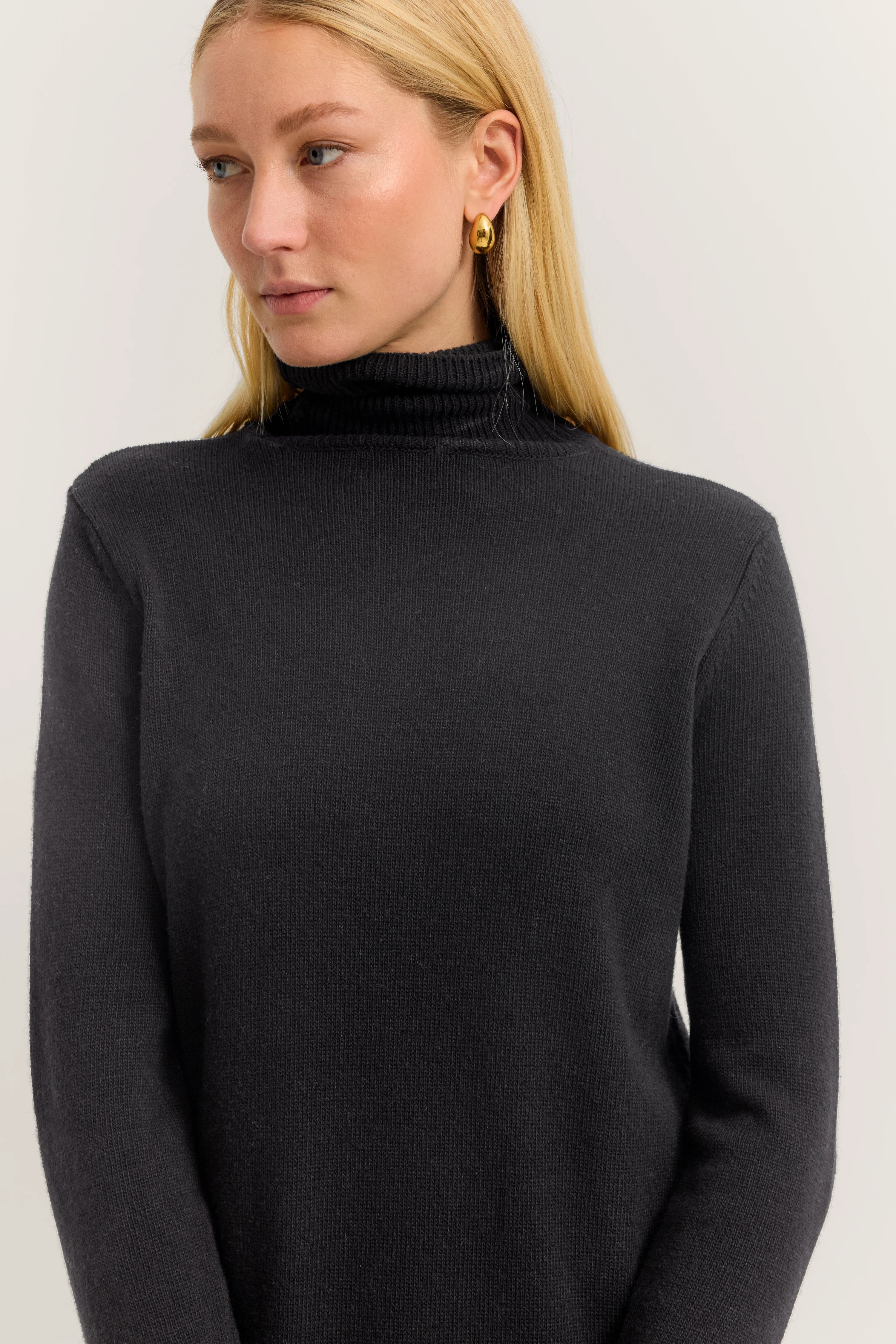 Black bugatti turtleneck sweater on model, side pose, simple and elegant.