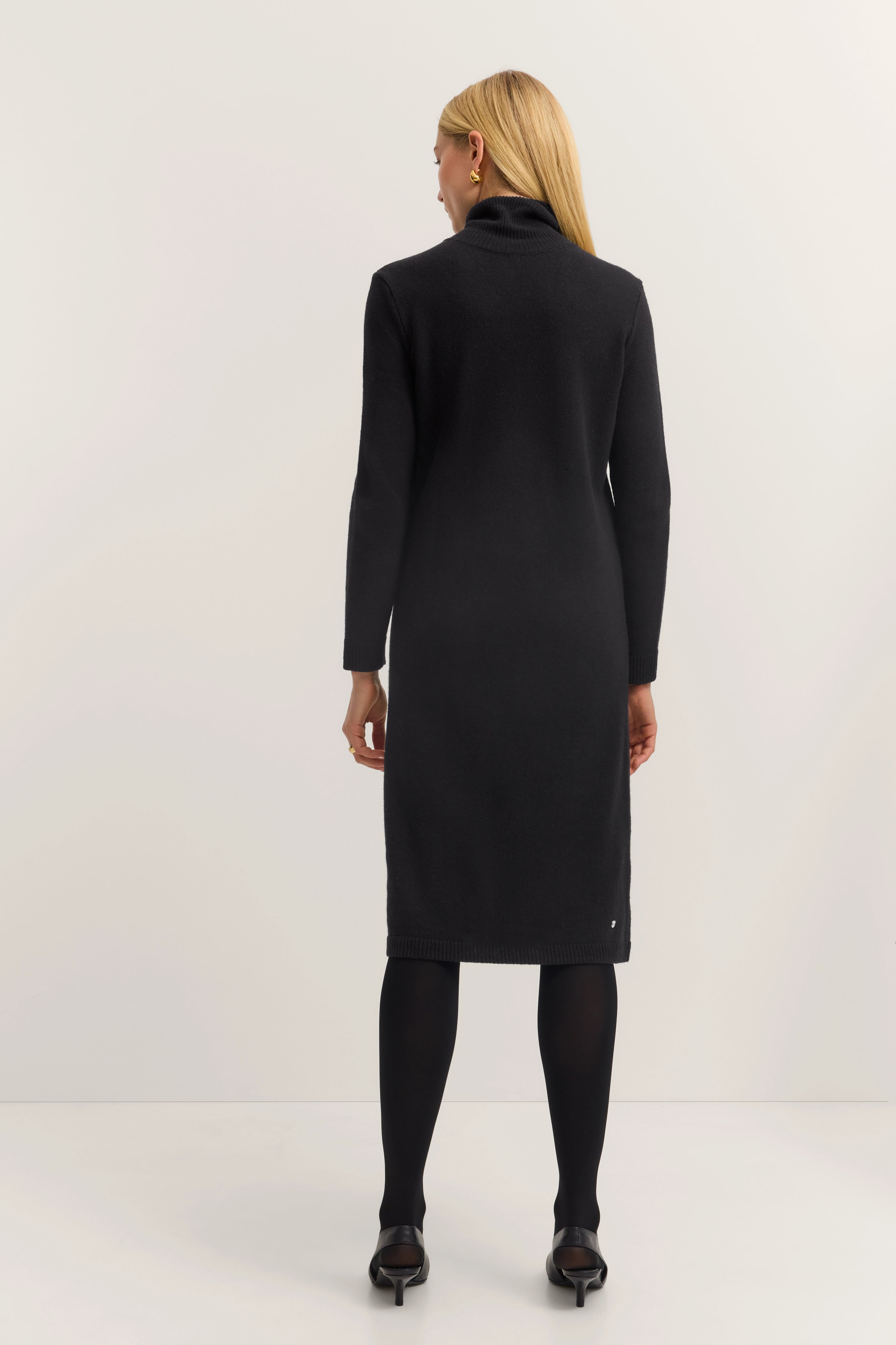 Rear view of model in black bugatti knit dress, standing elegantly, timeless style.