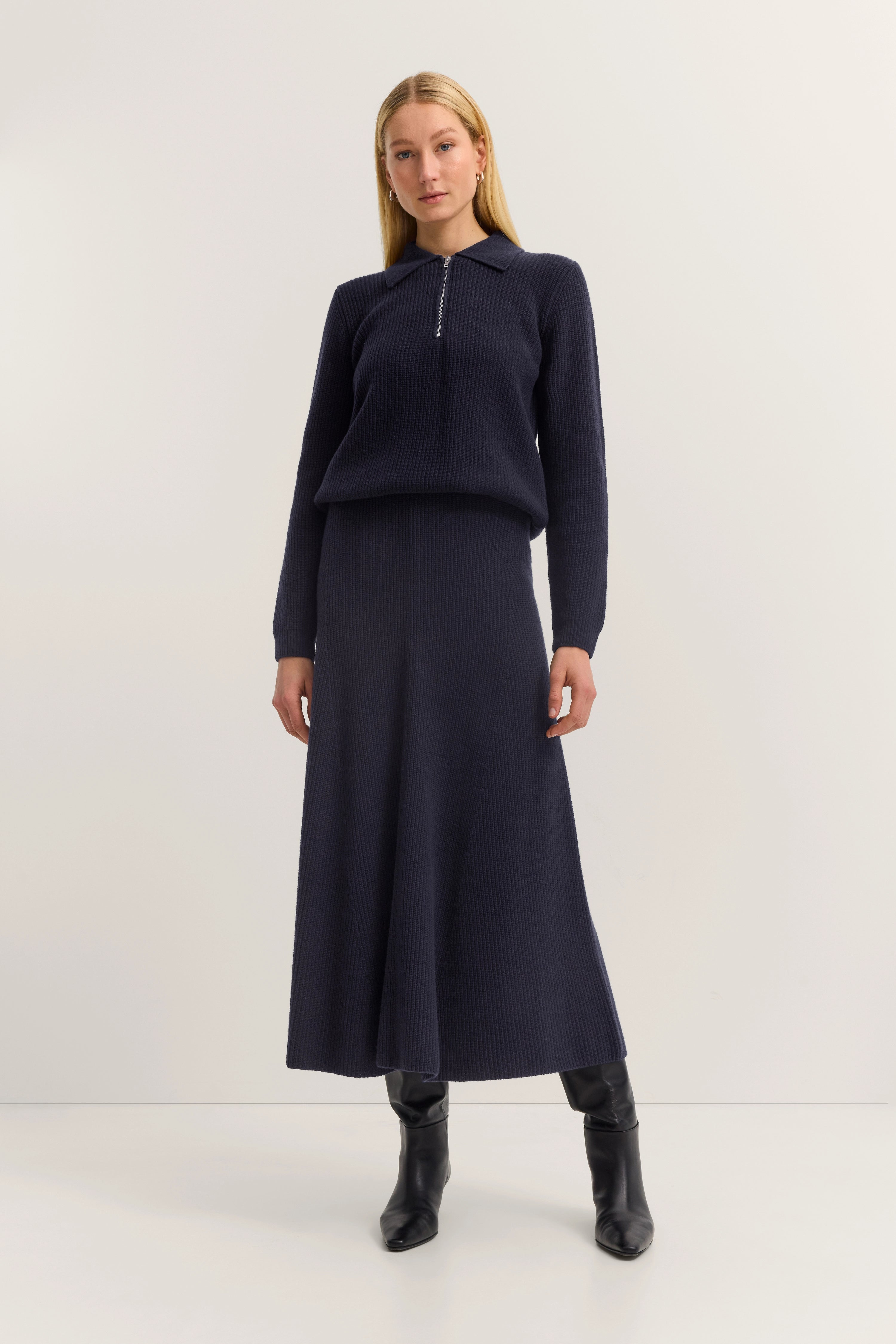 Navy Strickkleid mit Reißverschluss von bugatti, schwarzer Stiefel, Model steht entspannt.
