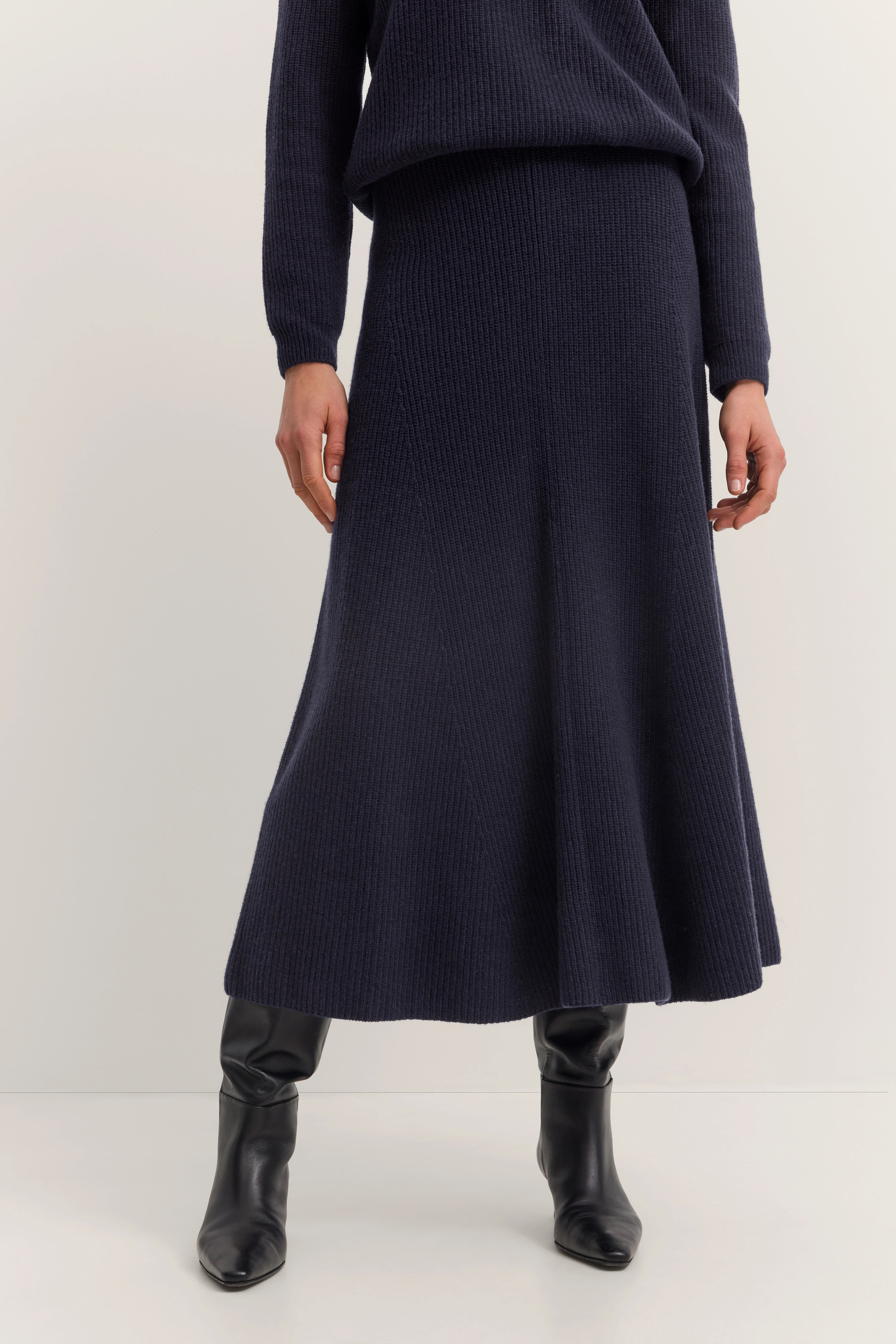 Dunkelblaues Strickkleid mit Stiefeln, legeres Modelbild, entspannte Pose.