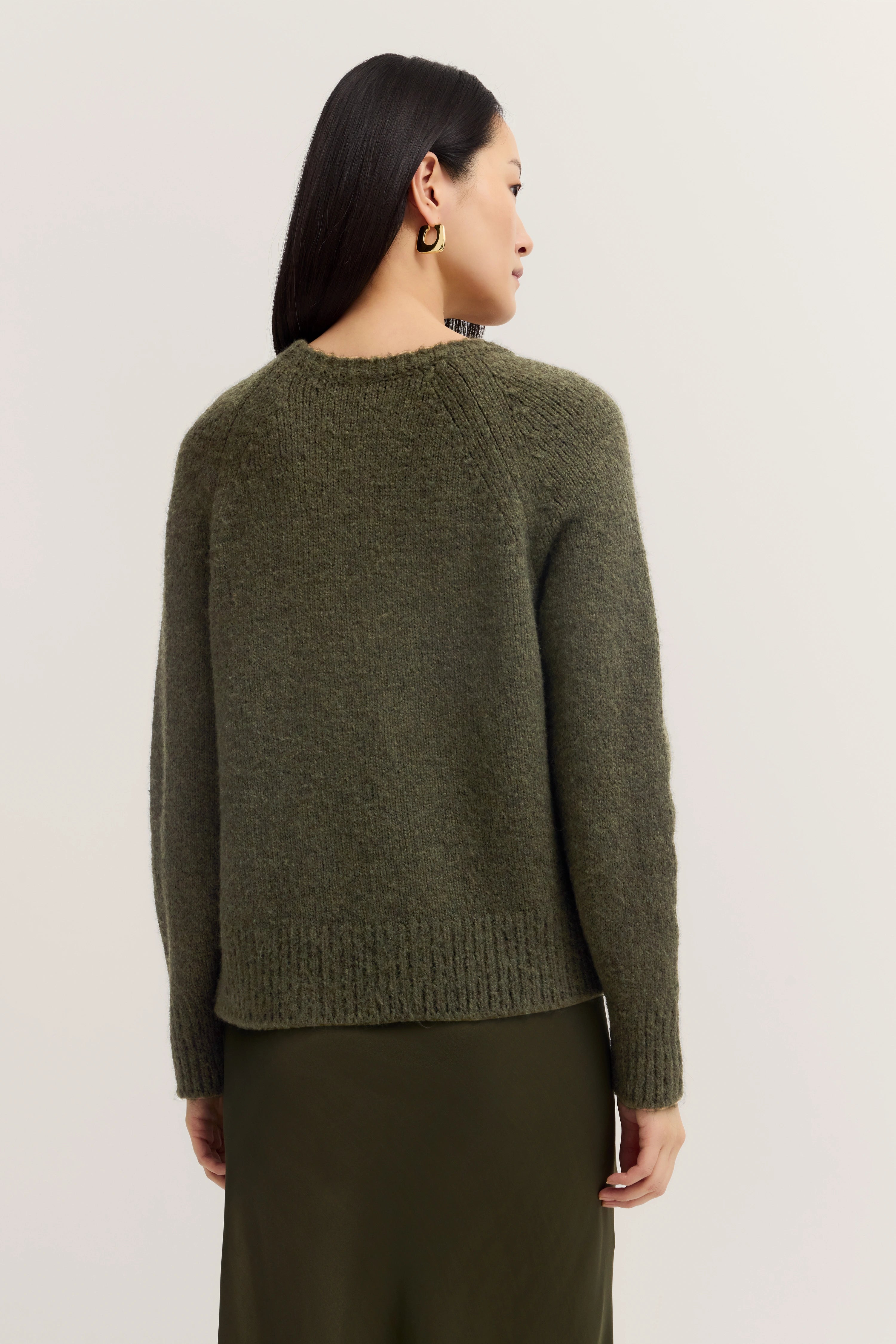 Rückansicht Modelbild mit olivgrünem Pullover und Rock, entspanntes Posing, stilvoll und gelassen.