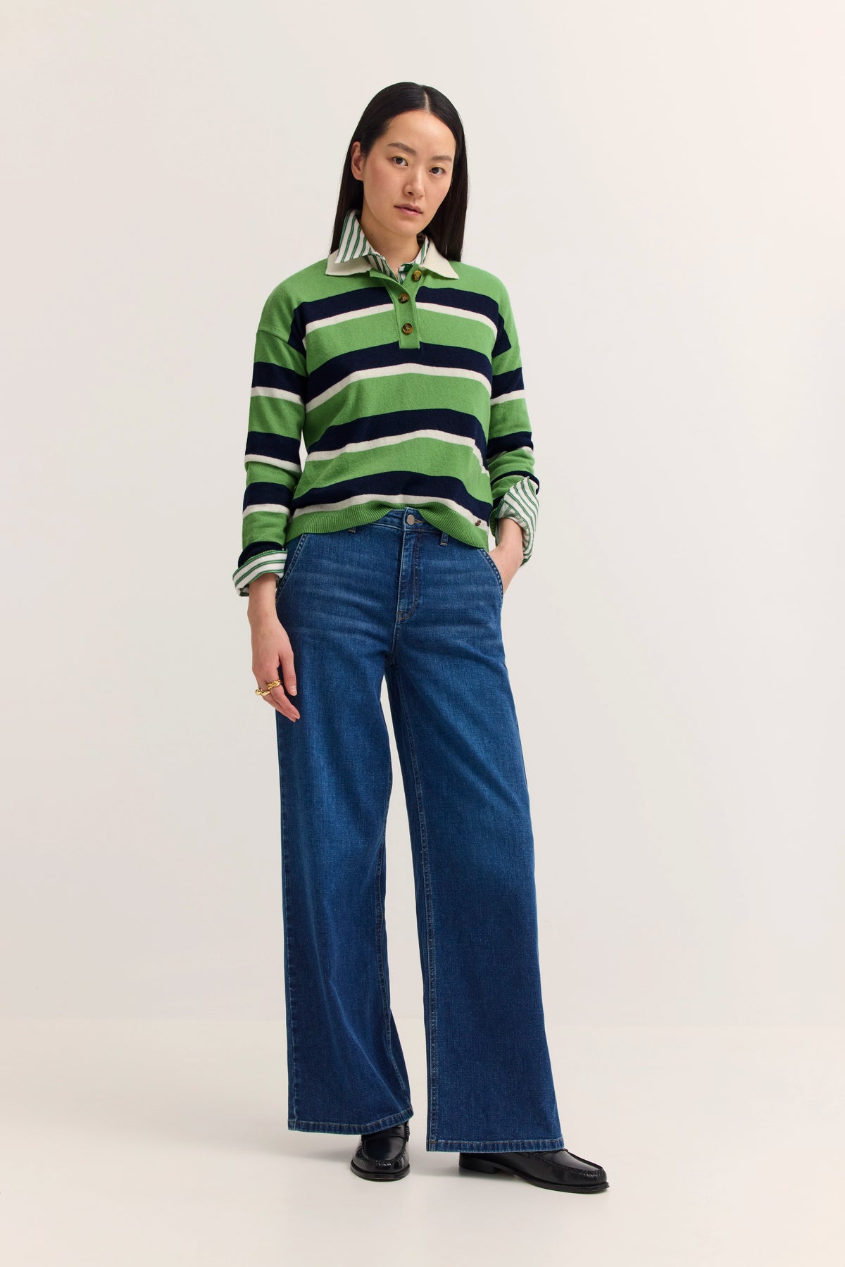 Grüner gestreifter Pullover, blaue Jeans, Model stehend, Hände in Taschen.