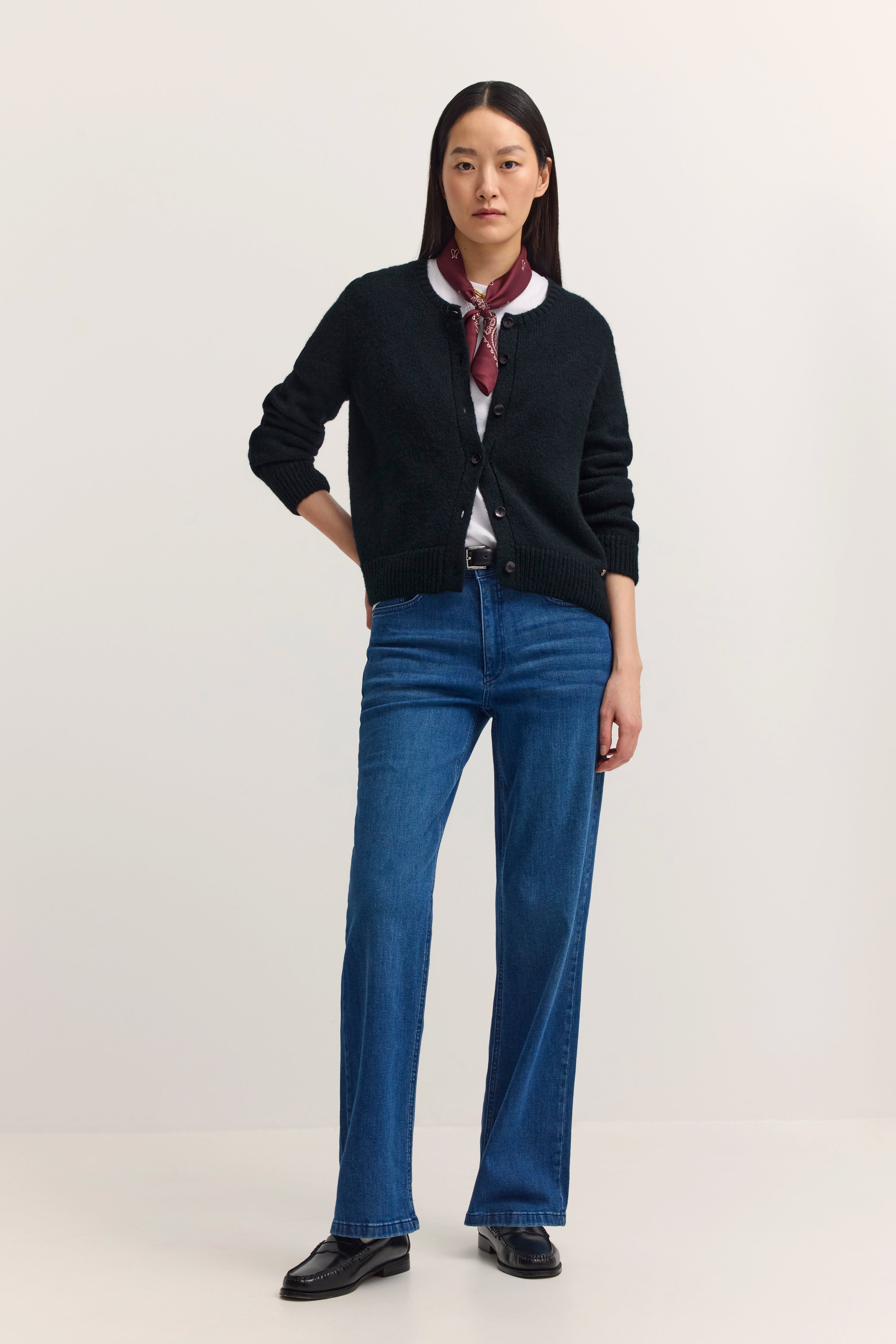 Dunkelgrüne Strickjacke über weißem Shirt, bordeauxrotes Halstuch, Büstenbild.