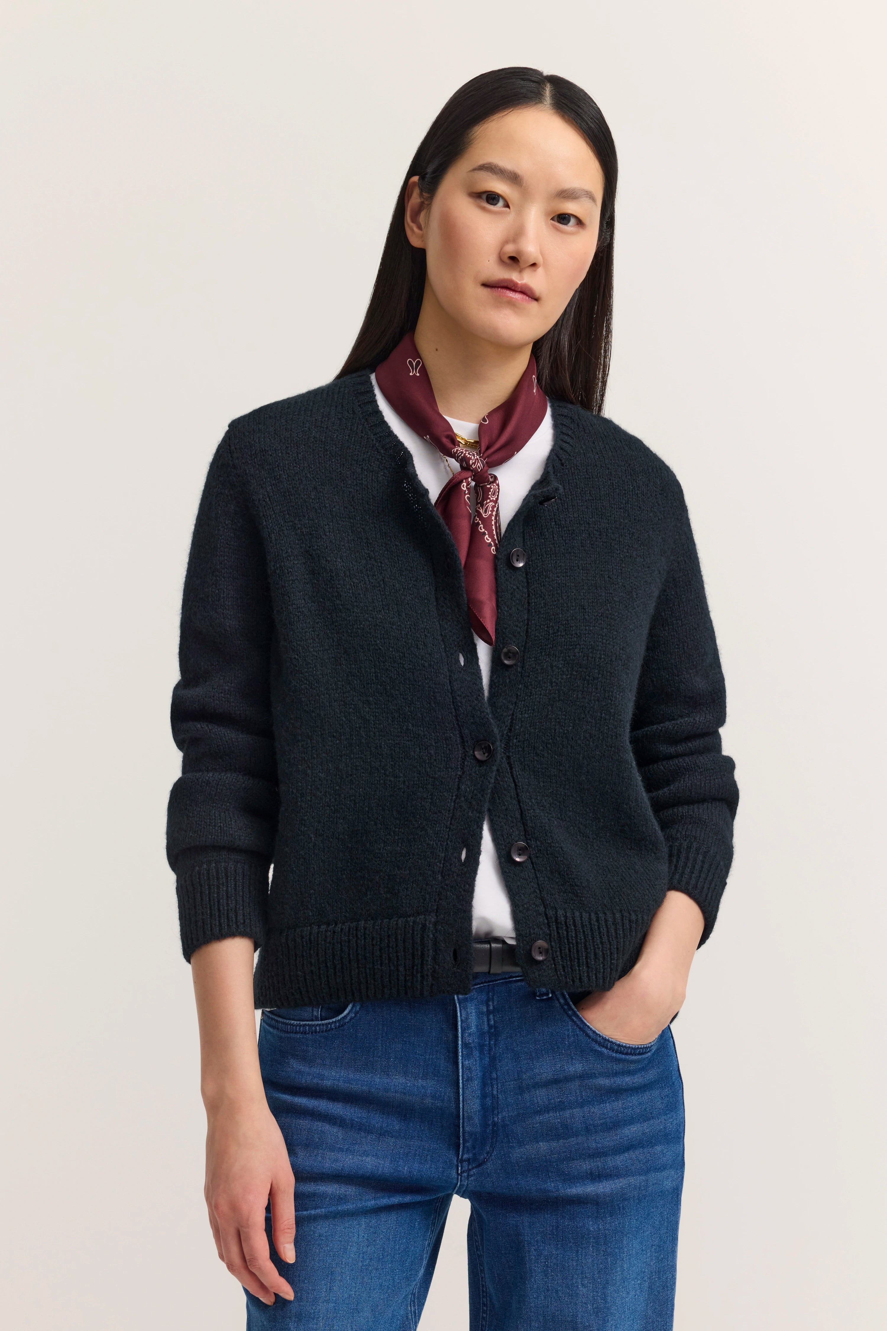 Model trägt schwarzen Cardigan, weißes Shirt, Jeans, bordeauxrotes Halstuch