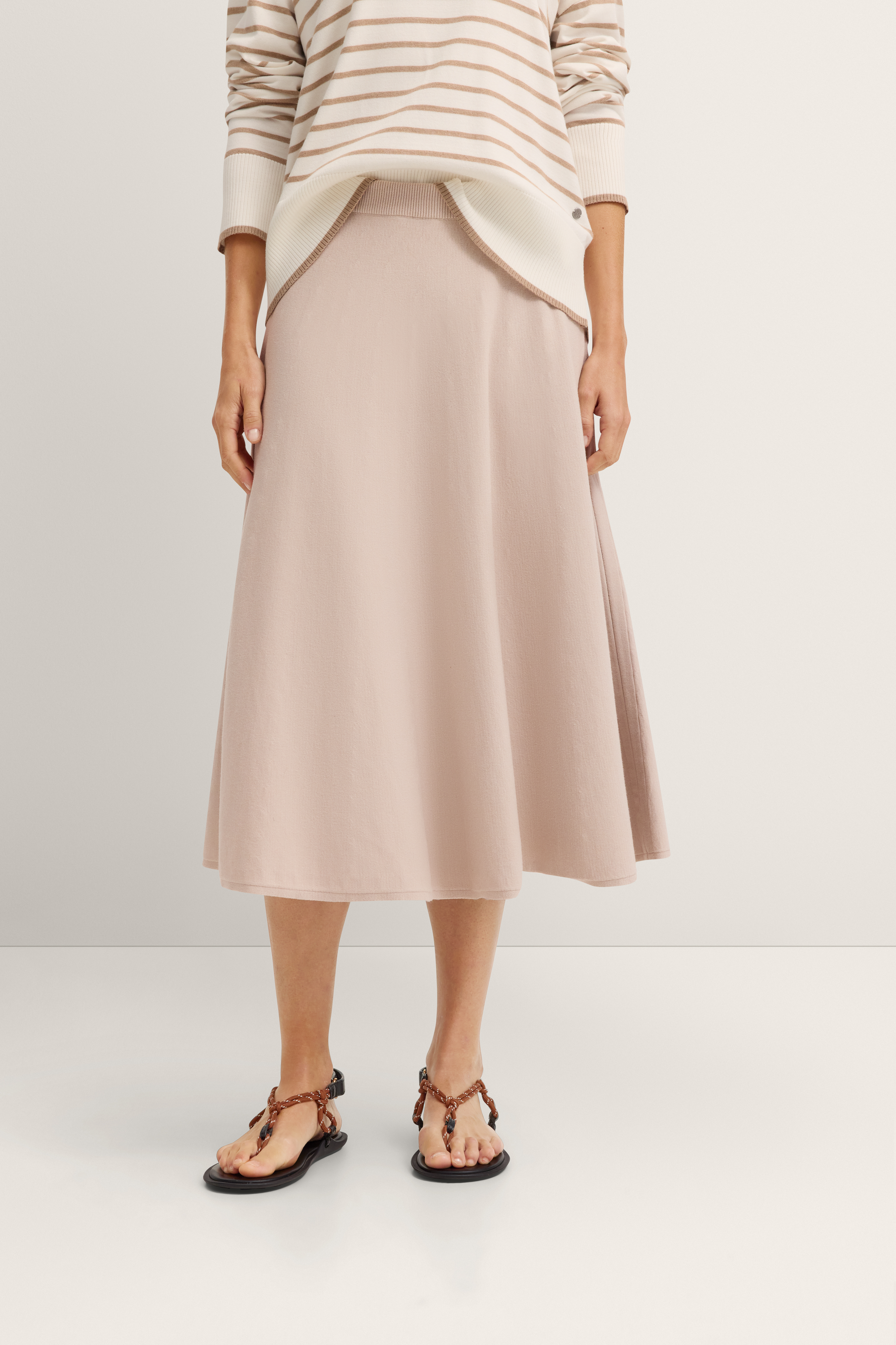 Beiger Rock mit gestreiftem Pullover, legeres Modelbild, entspannte Pose.