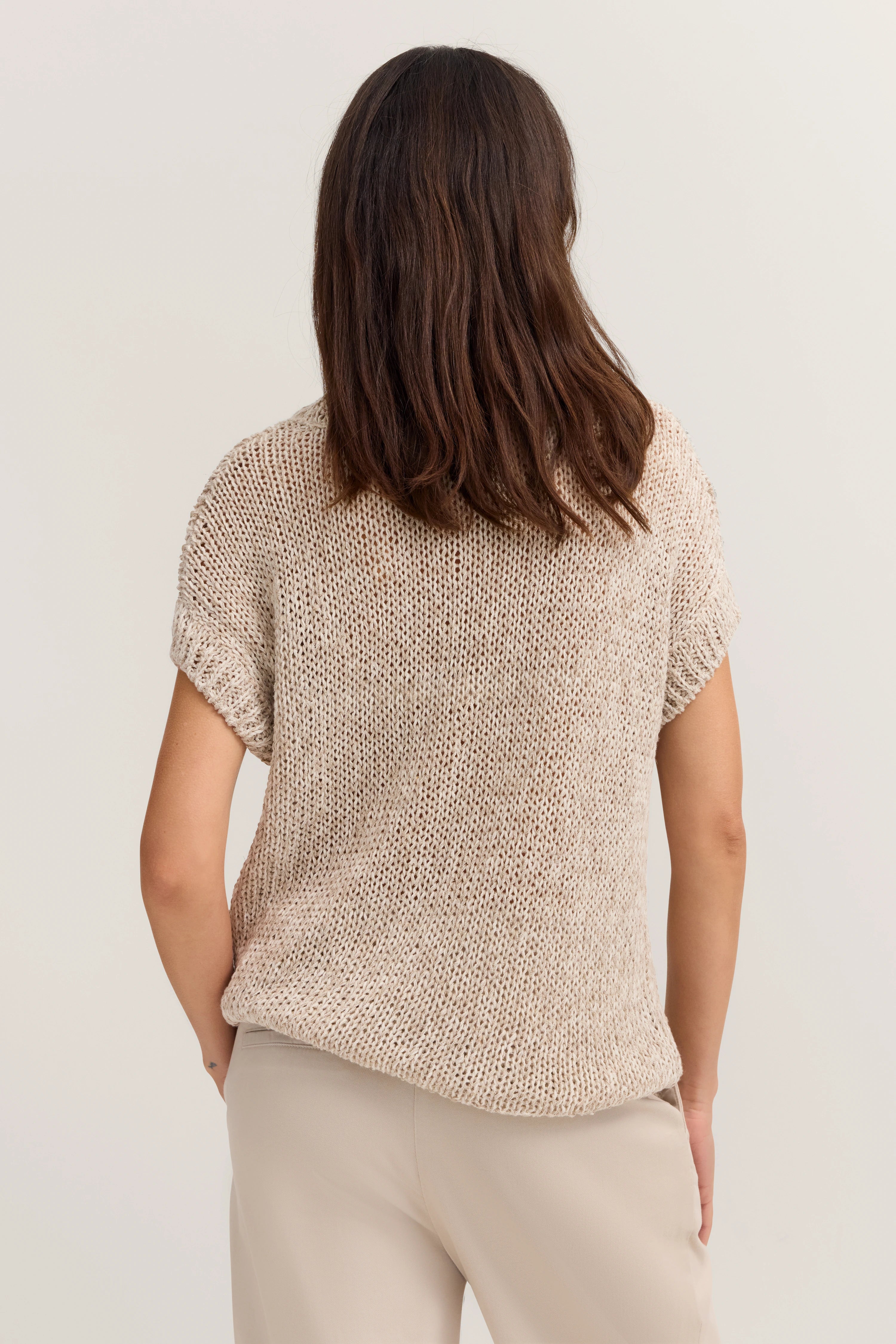 Beiger Strickpulli und helle Hose in legerem Modelbild, Rückansicht.
