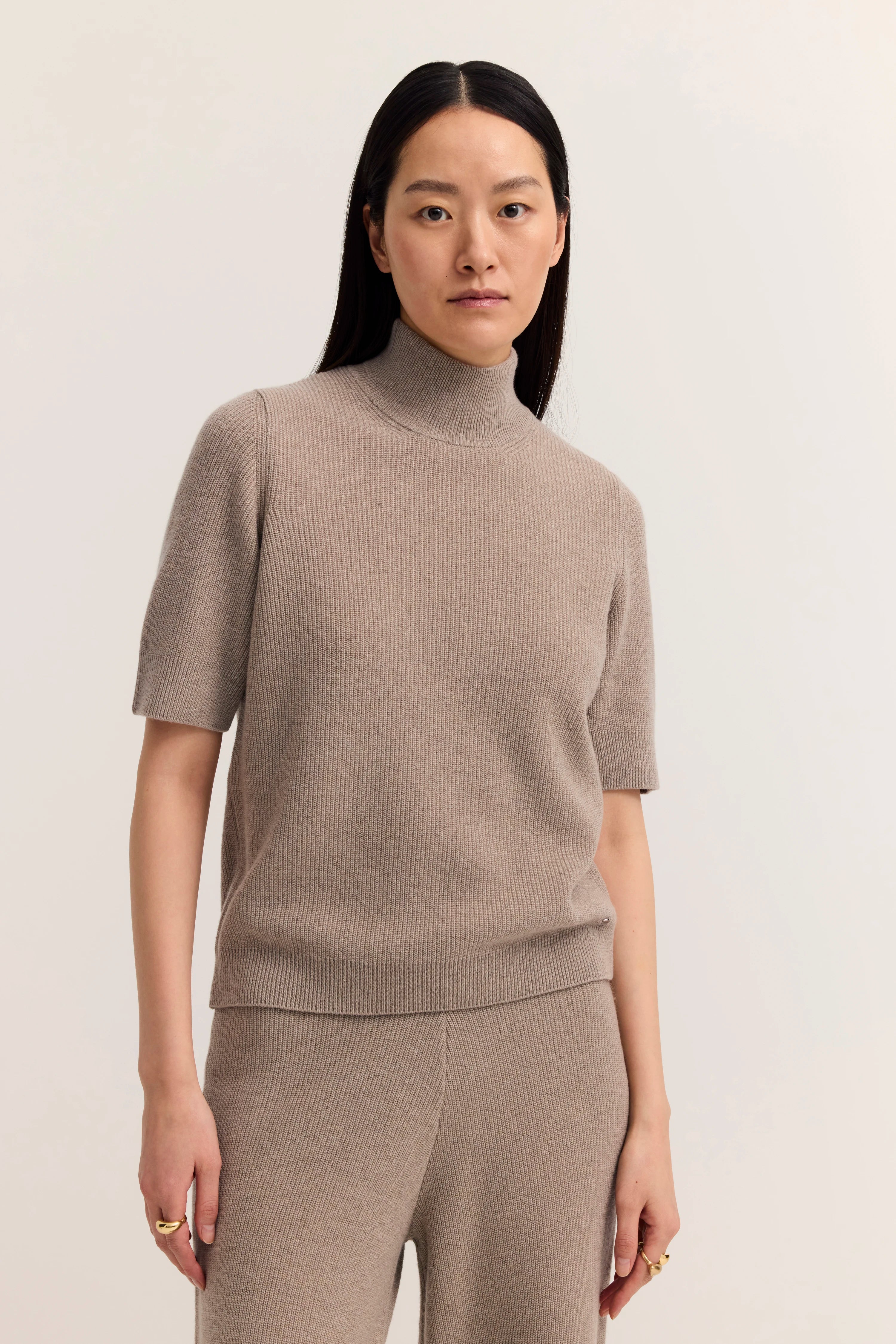 Model in taupefarbenem Strickset mit kurzem Arm, Büstenbild, lässige Pose.