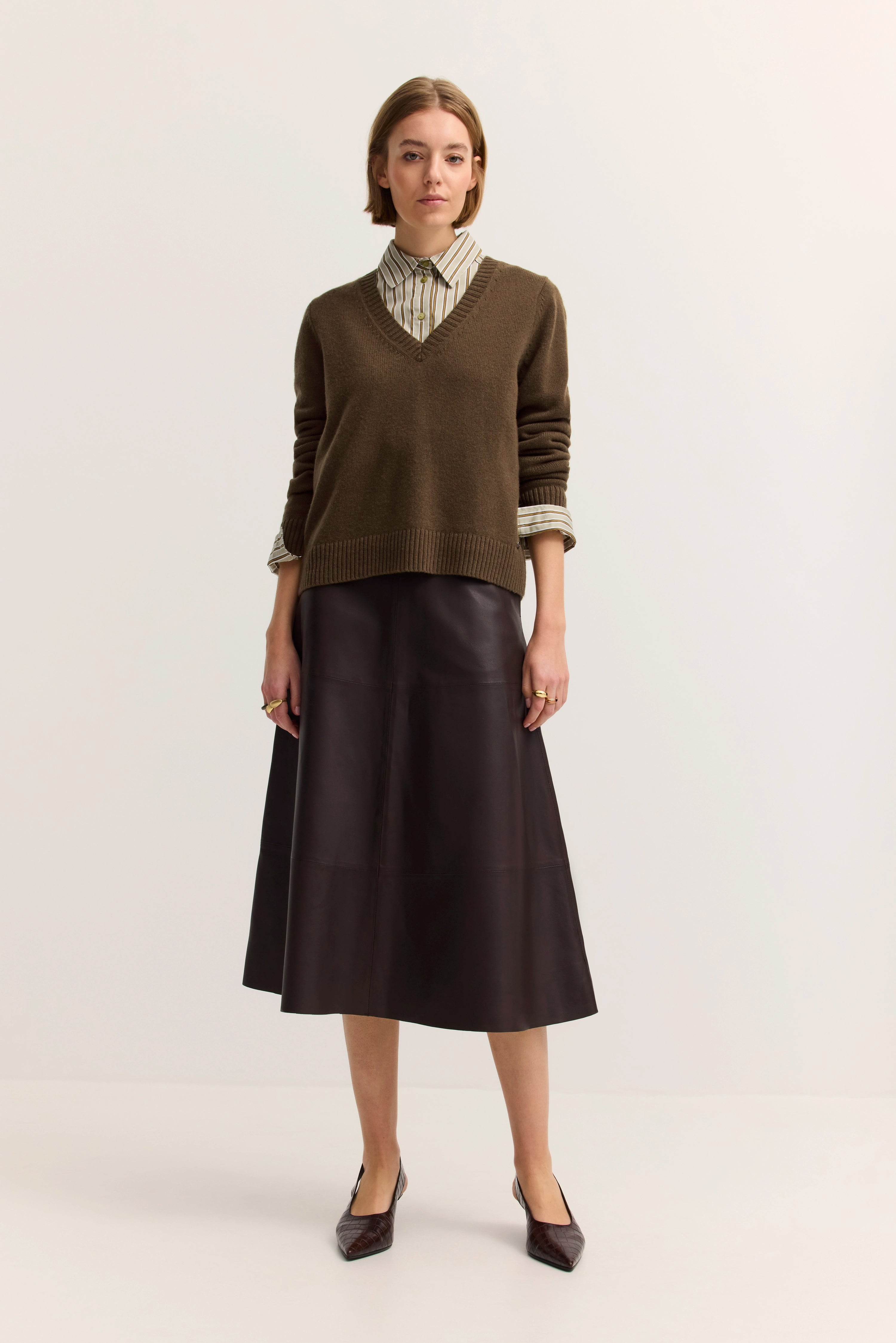 Model in braunem Pullover, gestreifter Bluse und Lederrock, stehend, zeitloser bugatti-Stil.