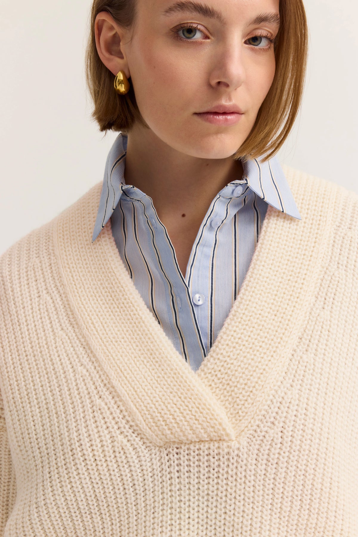 Beigefarbener Strickpullover, lässig getragen, mit blauer Hemdkragen-Applikation, Modell von hinten.