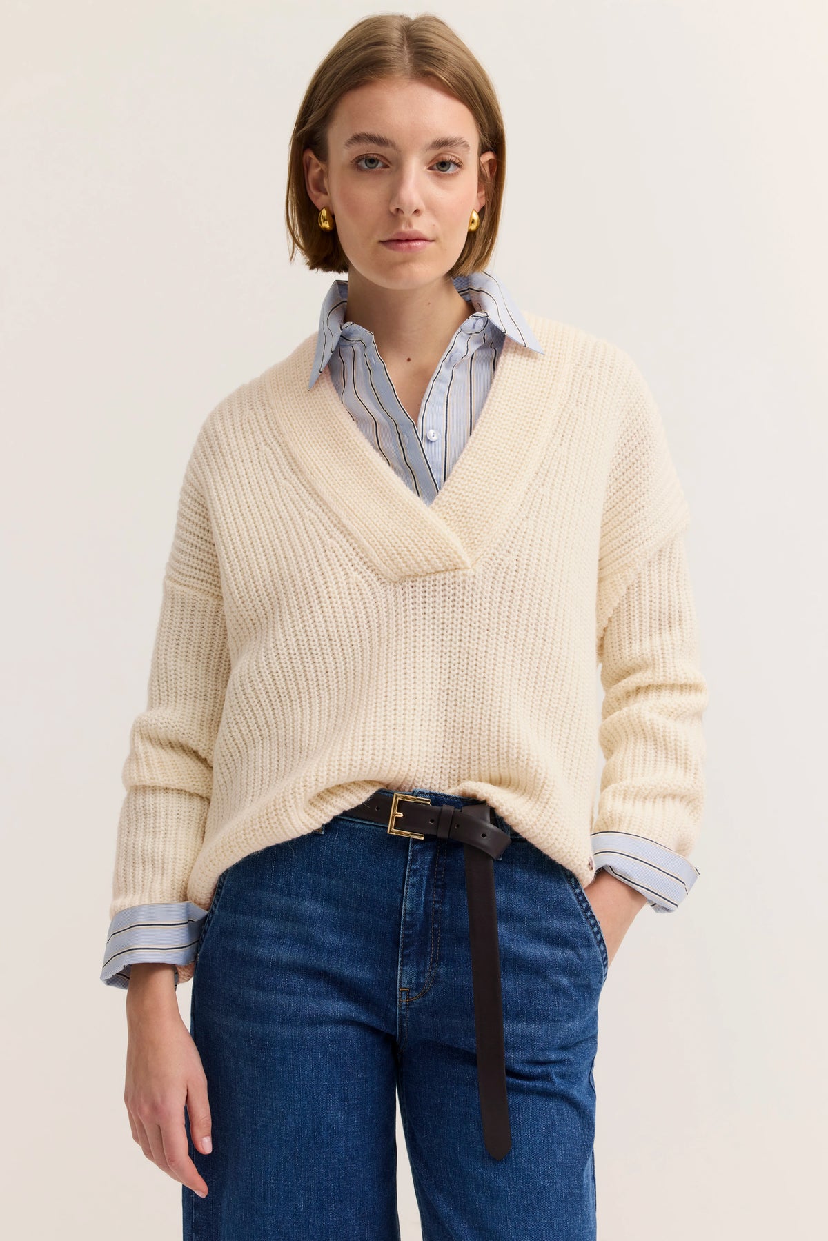 Beiger Strickpullover über gestreiftem Hemd, blaue Jeans