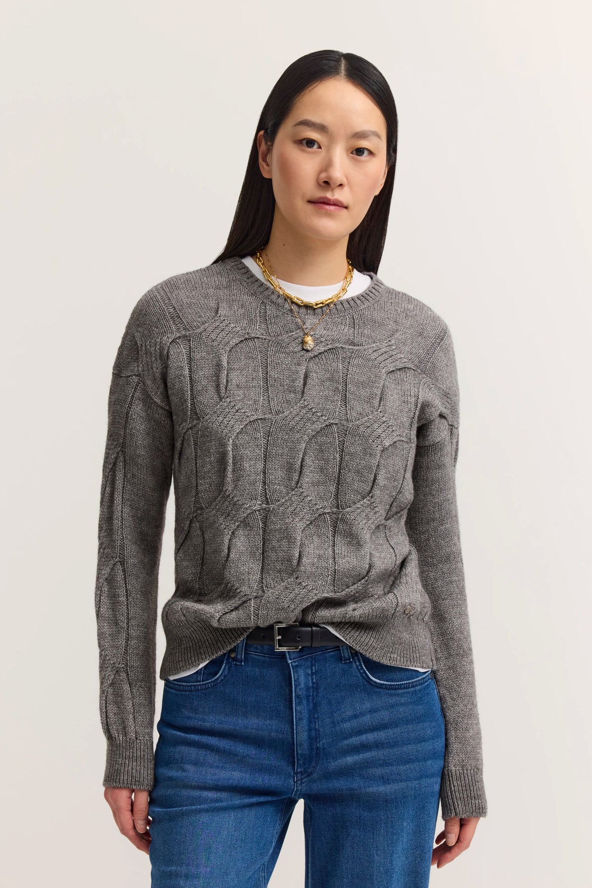 Grauer Strickpullover mit Muster, blaue Jeans, Model stehend, natürlicher Look.