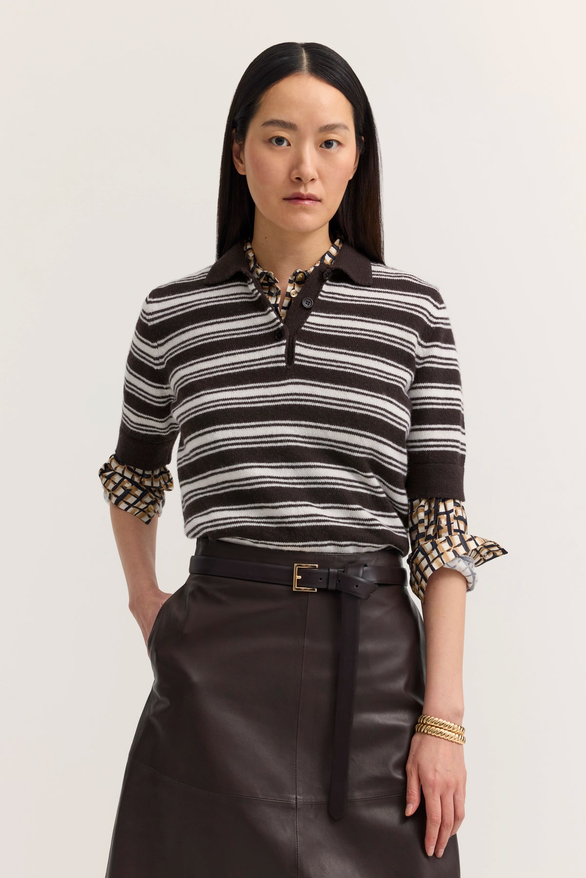 "Modelbild mit braun-weiß gestreiftem Polo, gemusterter Bluse und Lederrock