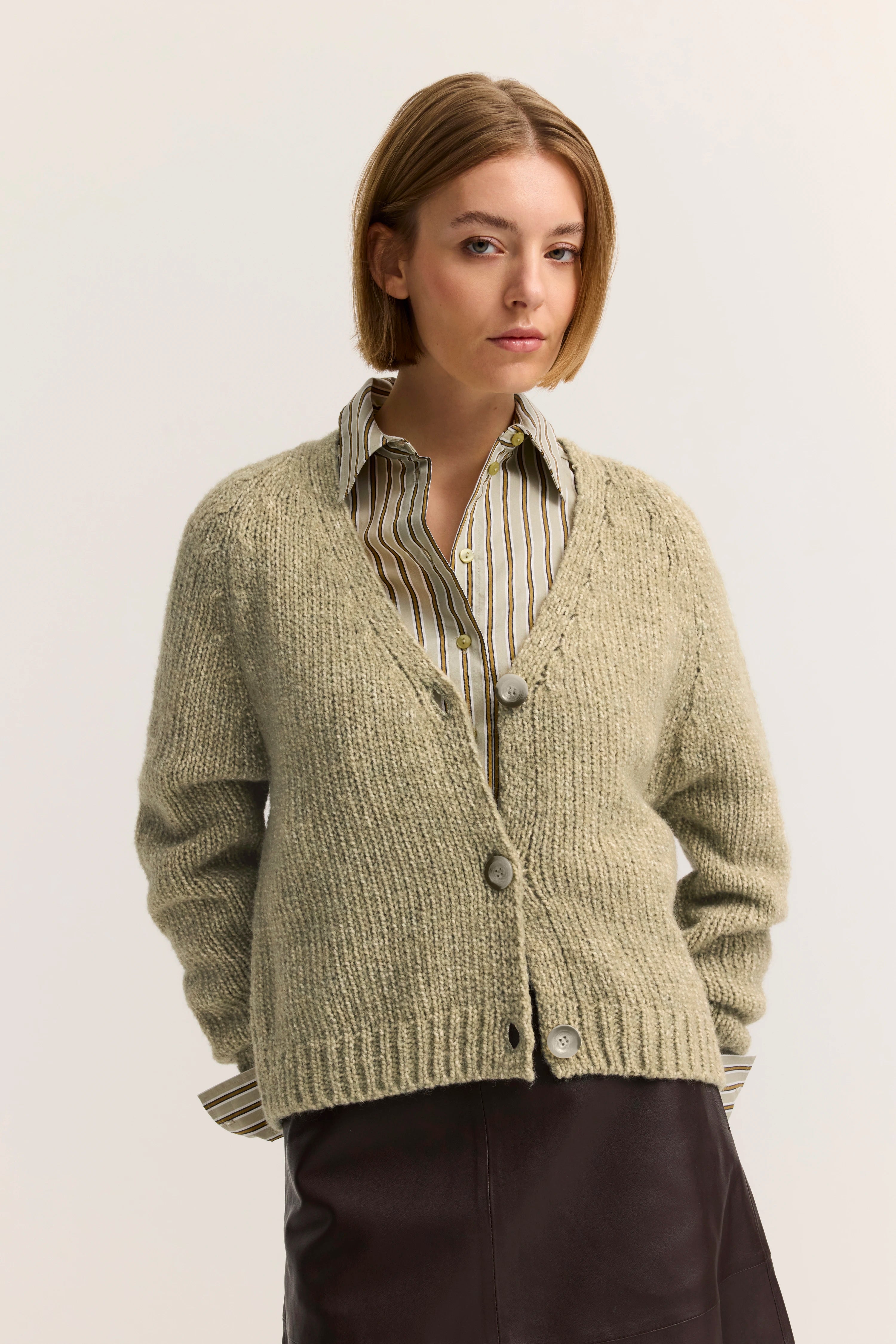 Alttext: Model trägt beigene Strickjacke über gestreifter Bluse, Lederrock