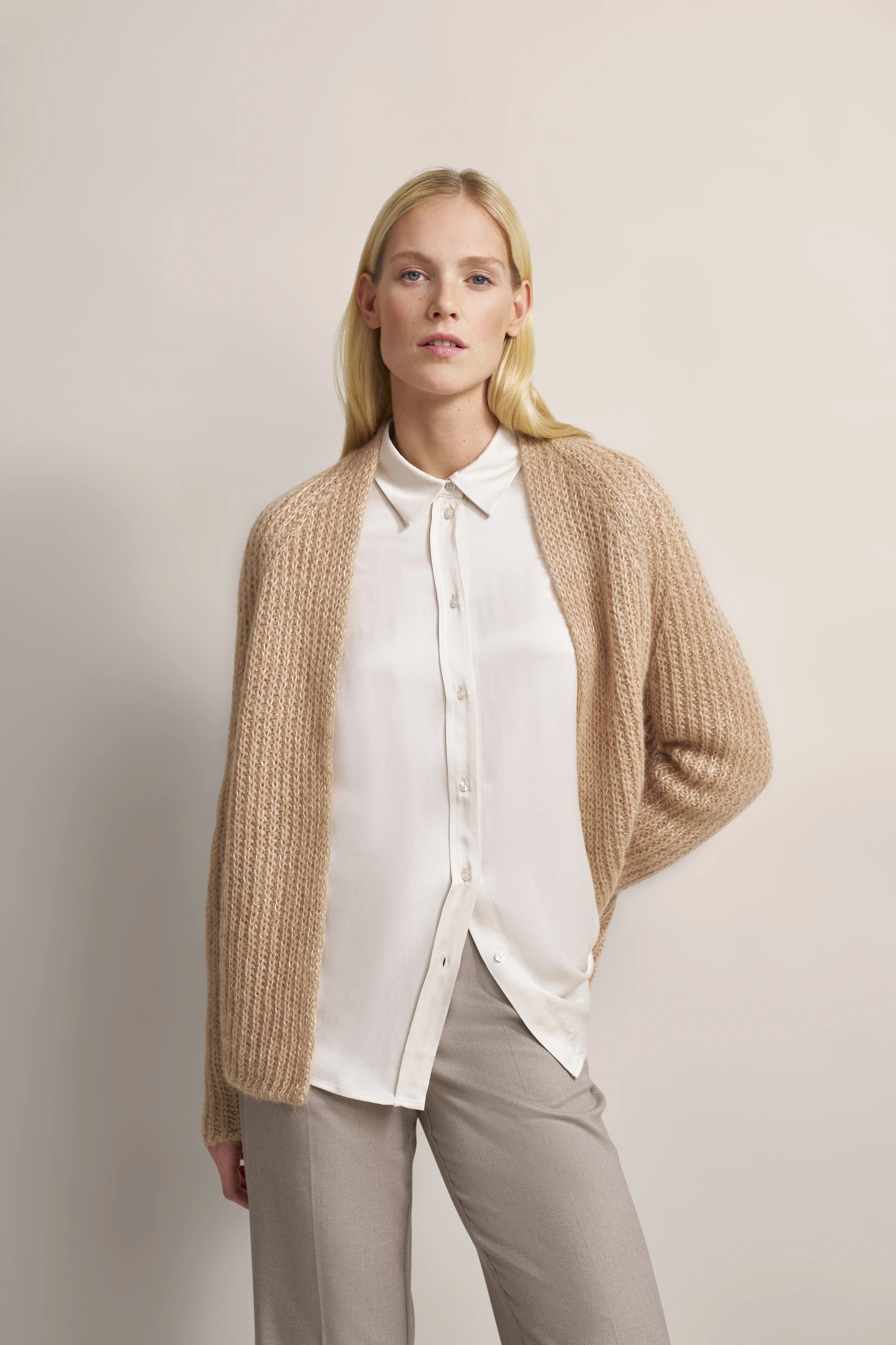 Model in beigem Cardigan, weißer Bluse und grauer Hose, entspannte Pose, bugatti Stil.