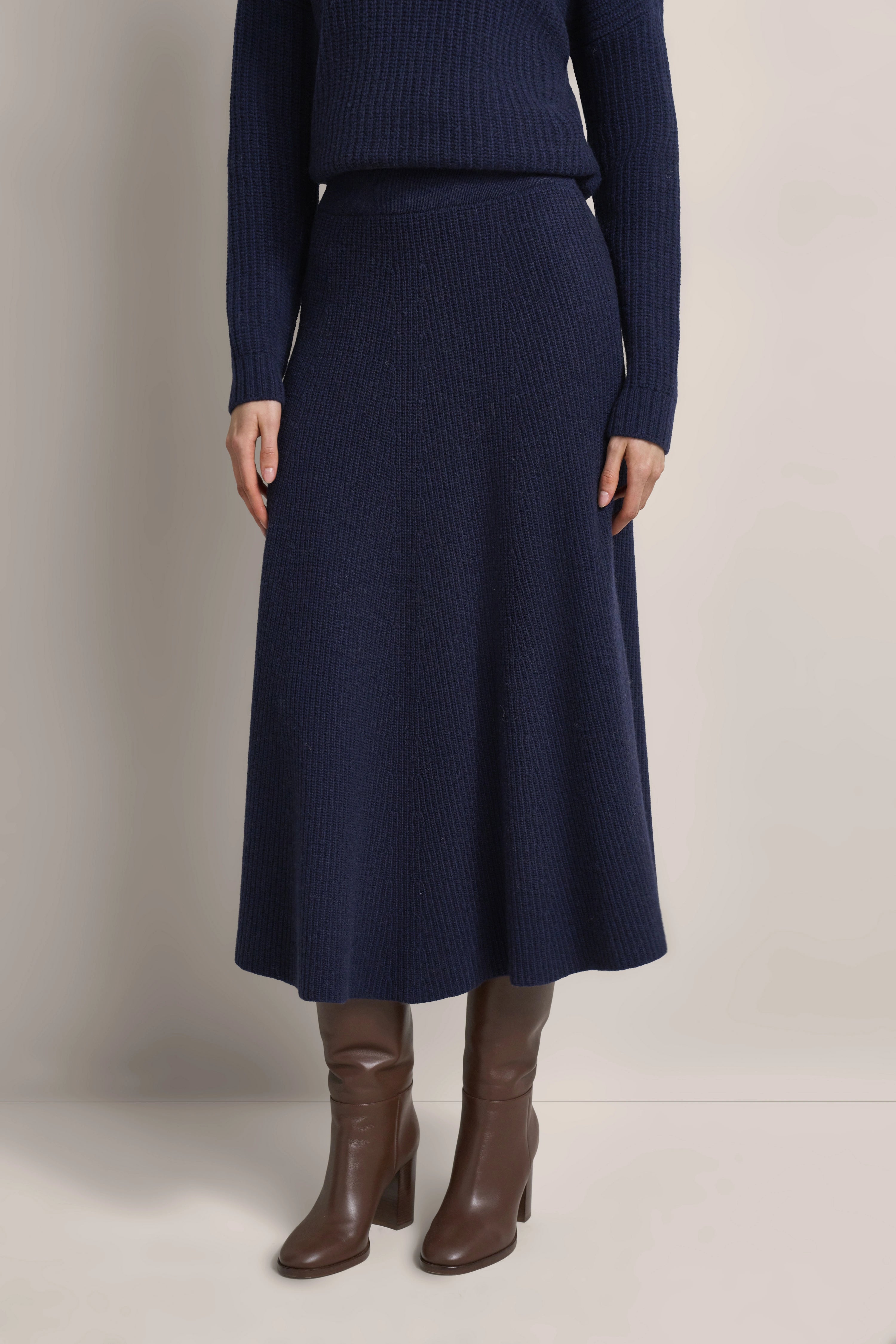 Dunkelblauer Strickpullover und Rock mit braunen Stiefeln, legeres Modelbild, stehende Pose.