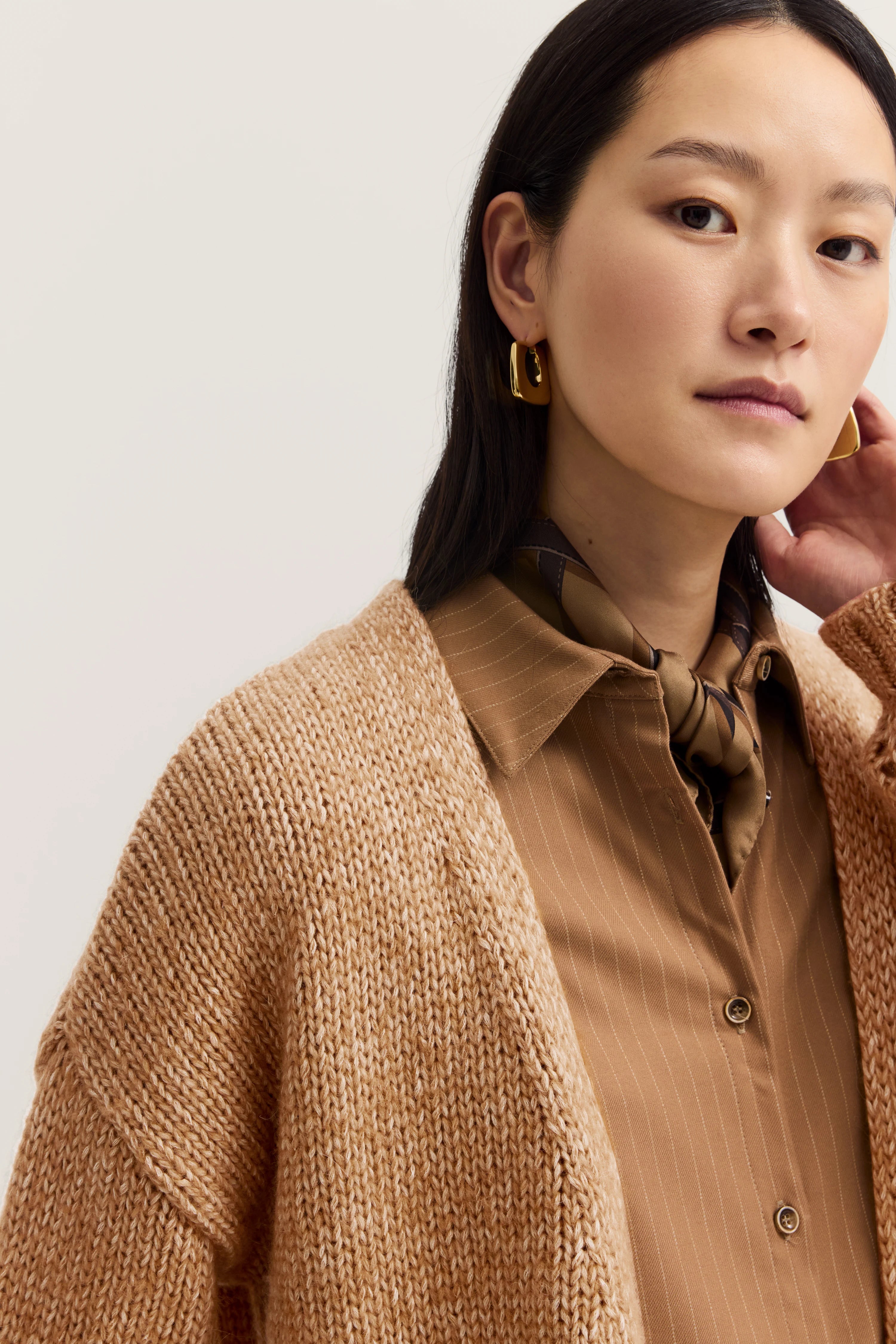Model in beigem Strickcardigan, brauner gestreifter Bluse und Tuch. Nahaufnahme, goldene Ohrringe.