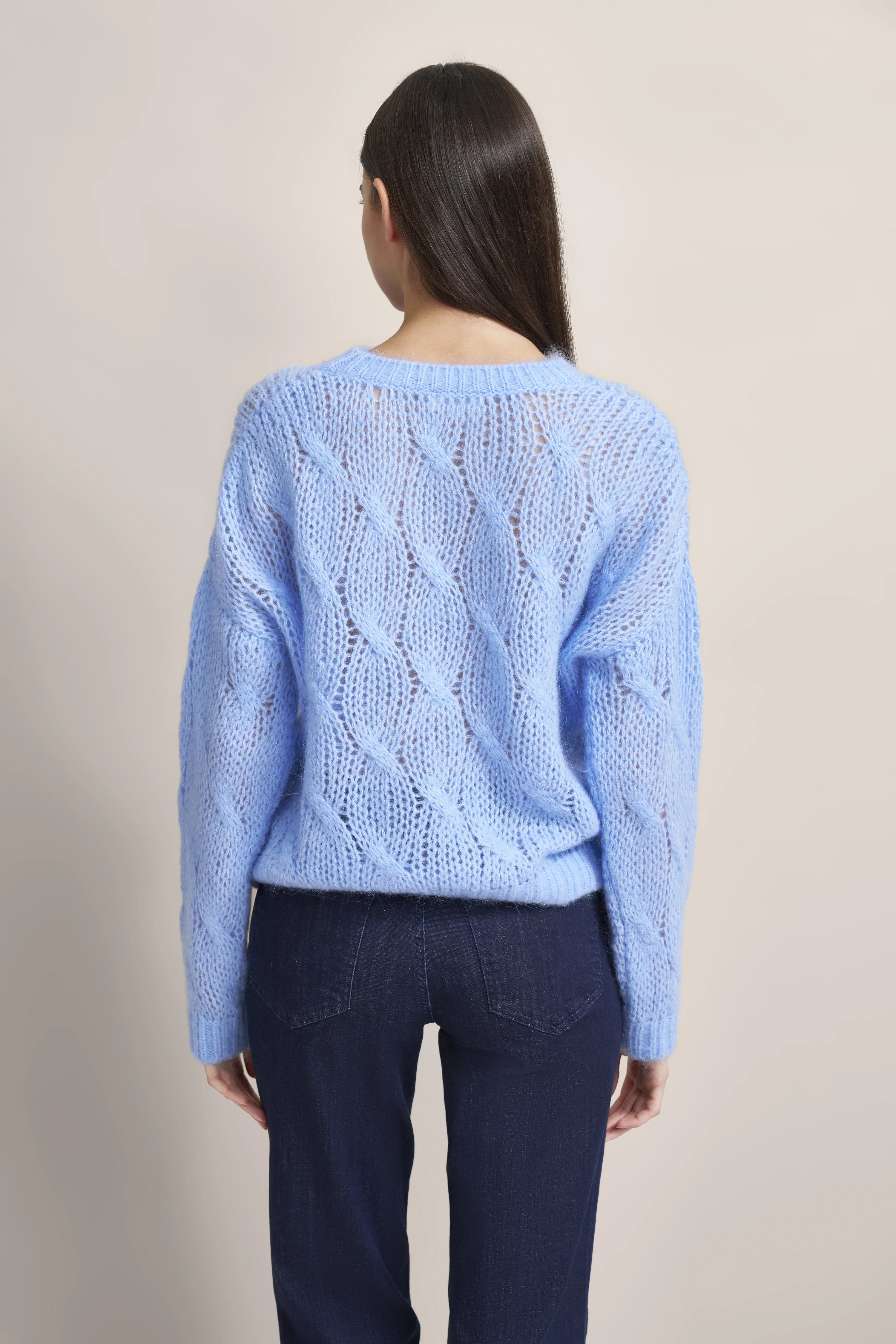 Strickpullover in Hellblau mit Zopfmuster, kombiniert mit dunkler Jeans. Model von hinten.