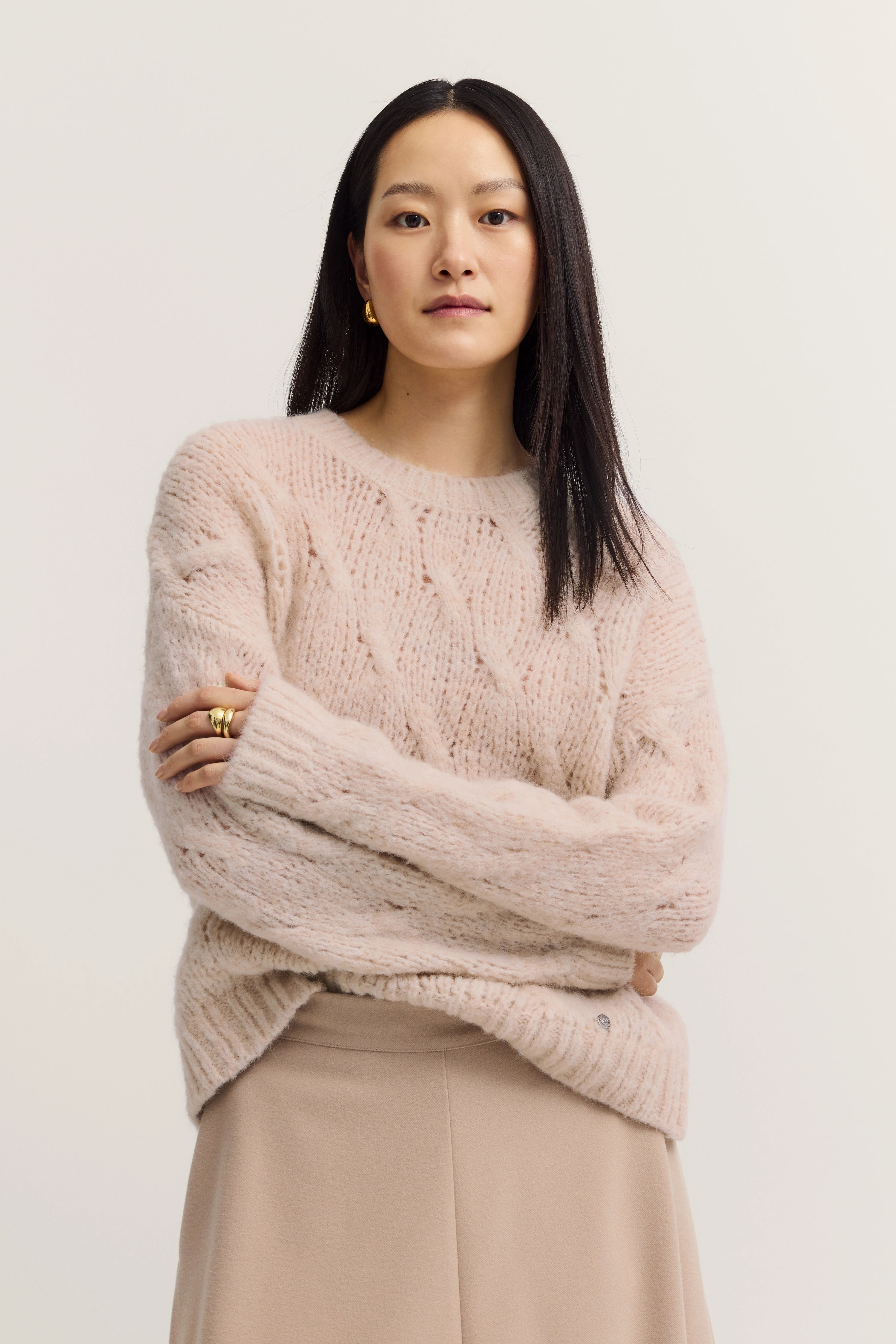 Beigefarbener Strickpullover und Rock, Modelbild mit verschränkten Armen, entspannter Ausdruck.