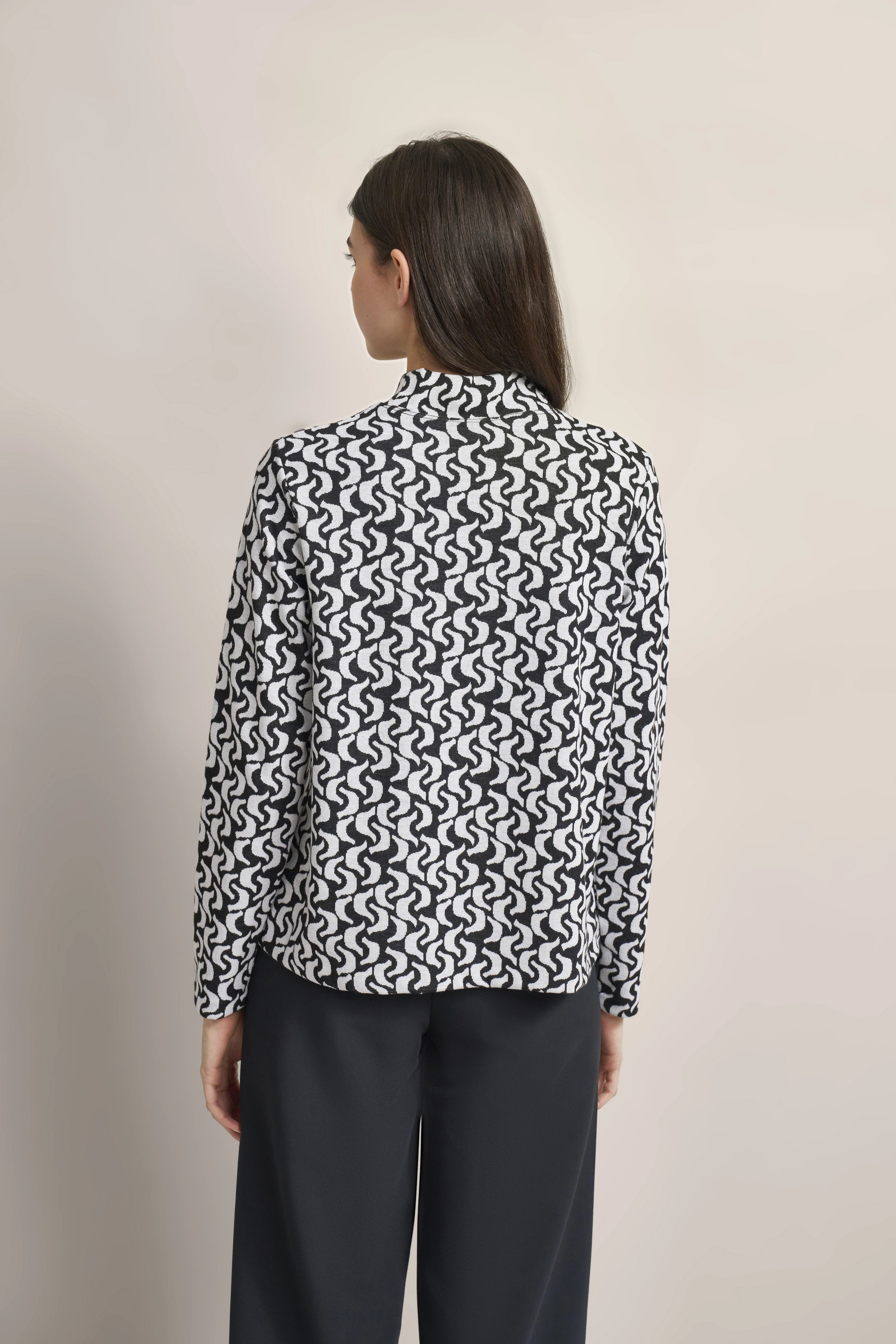 Model in schwarz-weiß gemusterter bugatti-Jacke und schwarzer Hose, Rückansicht.