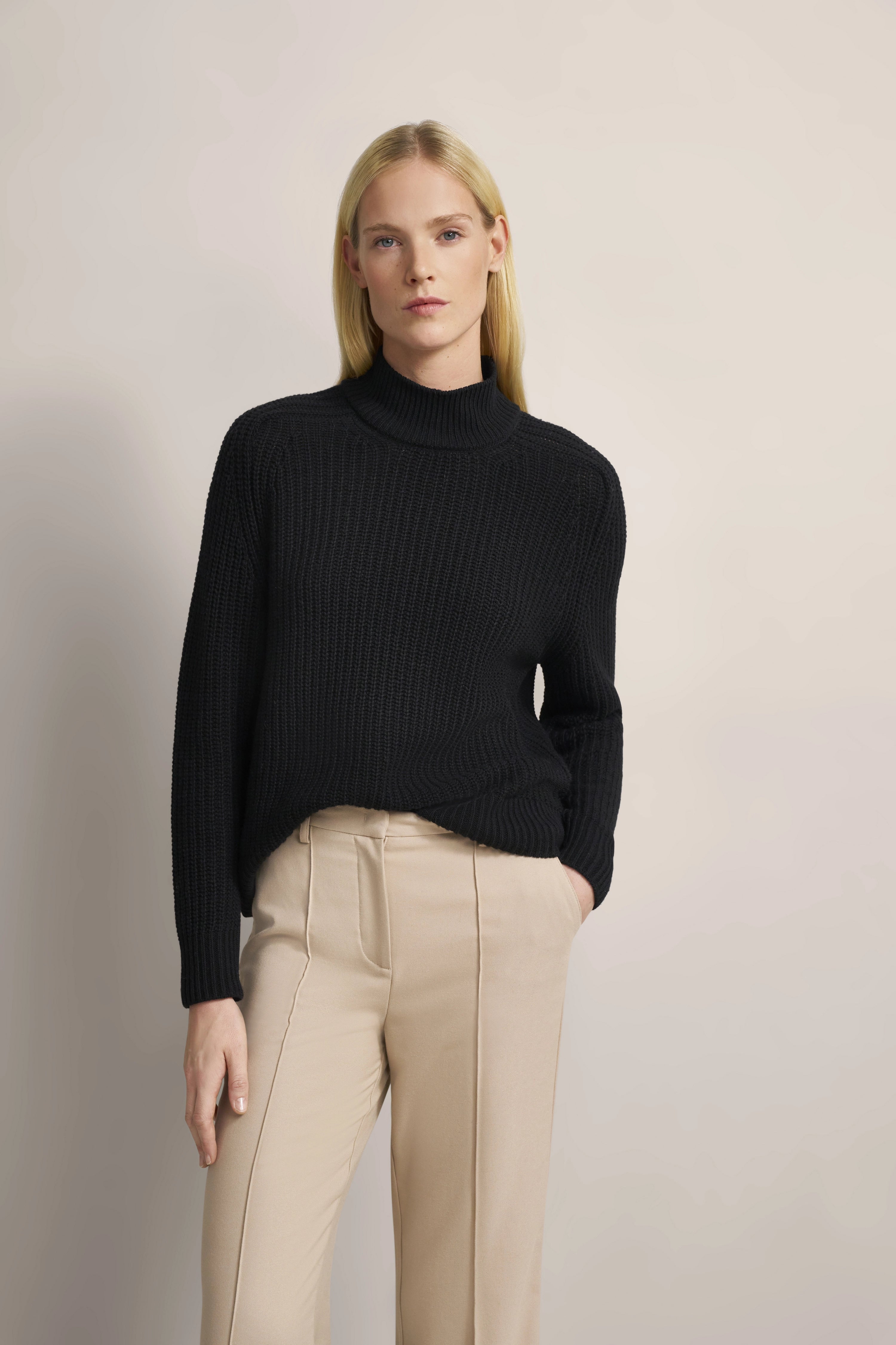 Schwarzer Strickpullover mit beigen Hosen, Modelbild, entspanntes Posing.